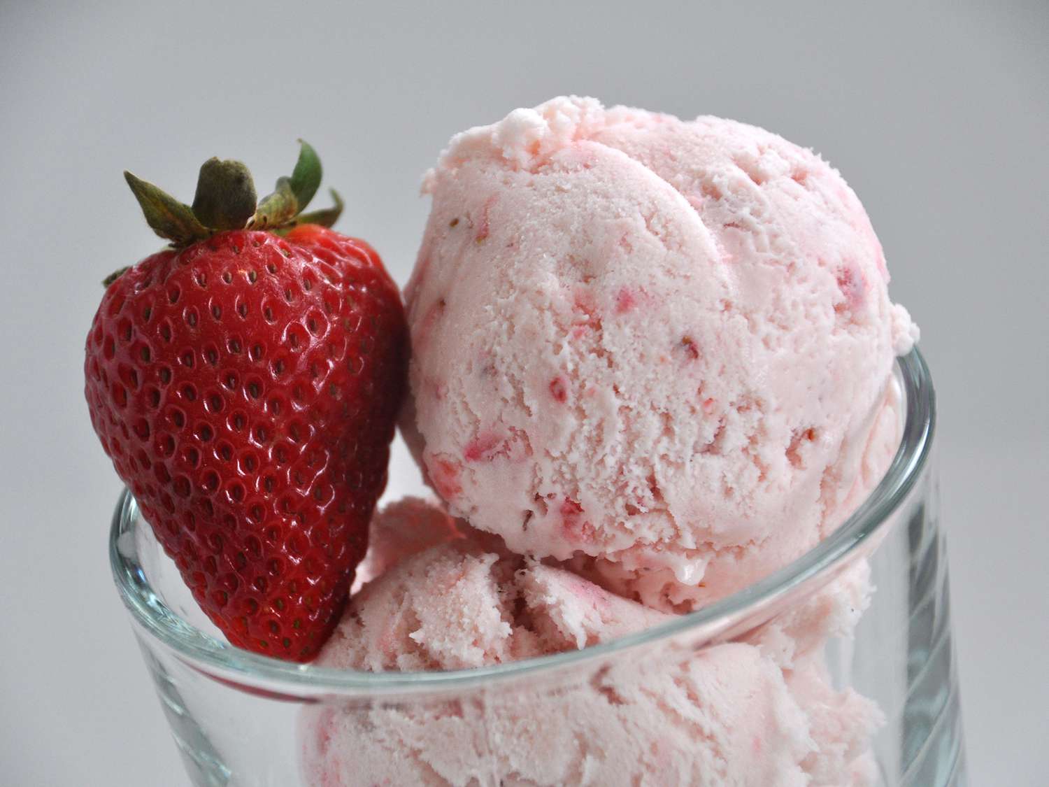 close up view of scoops of strawberry ice cream garnished with a strawberry in a glass