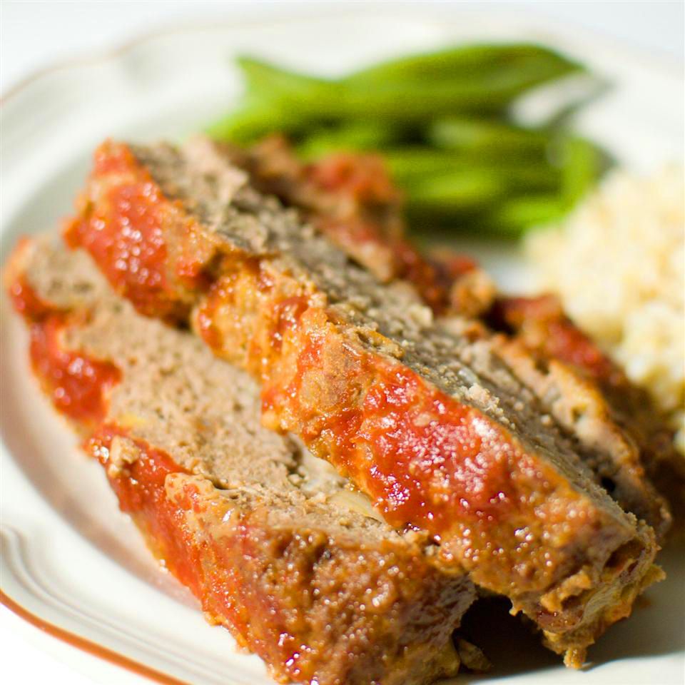 close up view of sliced Brown Sugar Meatloaf with green beans in the background on a plate