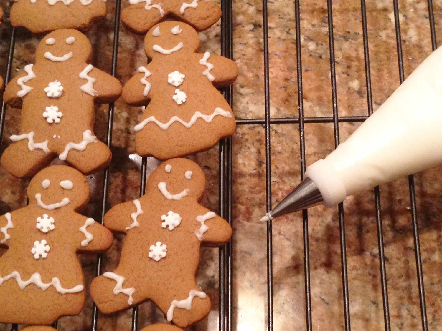 close up view of ginger bread men and Gingerbread Cookie Frosting in a piping bag, on a cooling rack