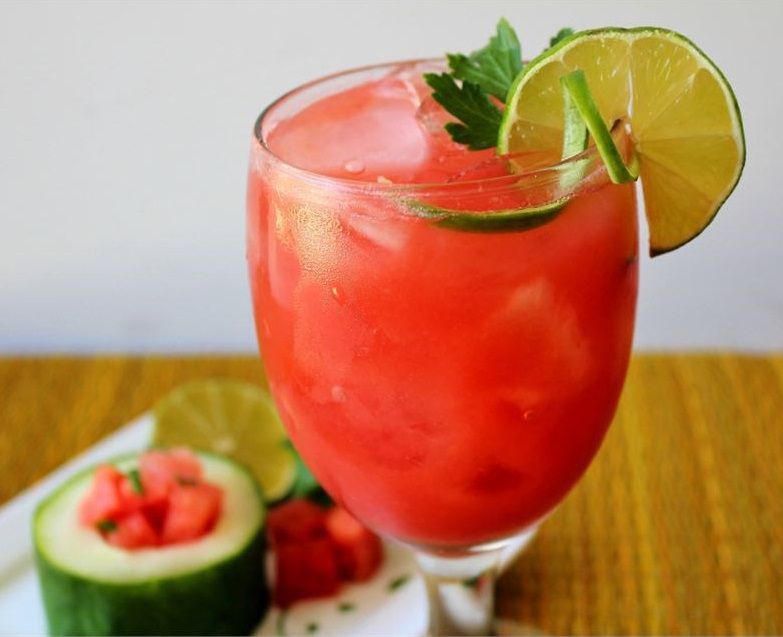 a stemmed glass holding bright pink watermelon juice garnished with a lime slice and fresh lime peel