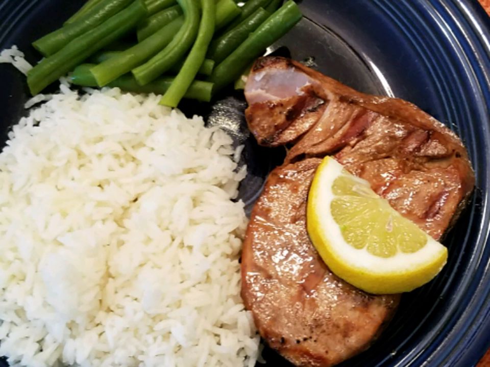 close up view of Grilled Yellowfin Tuna with Marinade garnished with lemon, on a blue plate with white rice and green beans