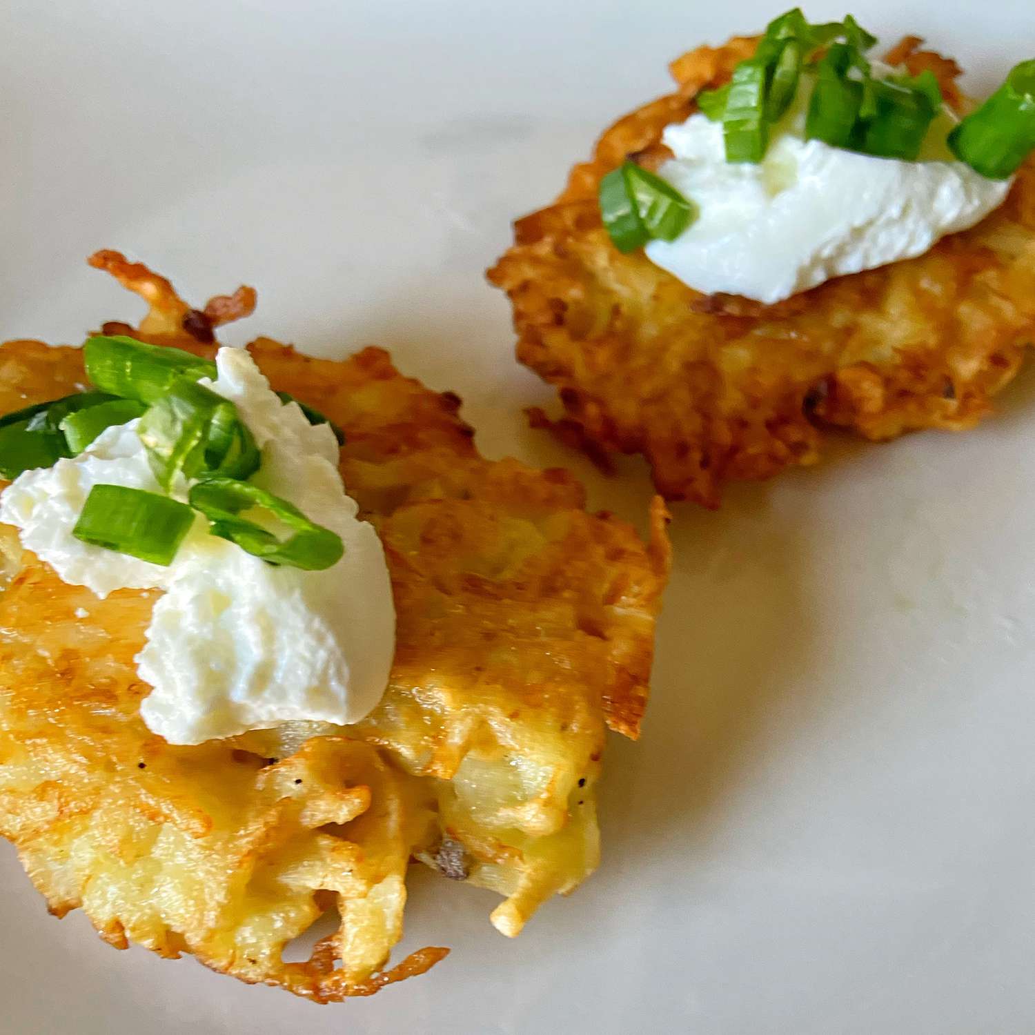 close up view of Potato Latkes garnished with sour cream and green onions on a whit plate
