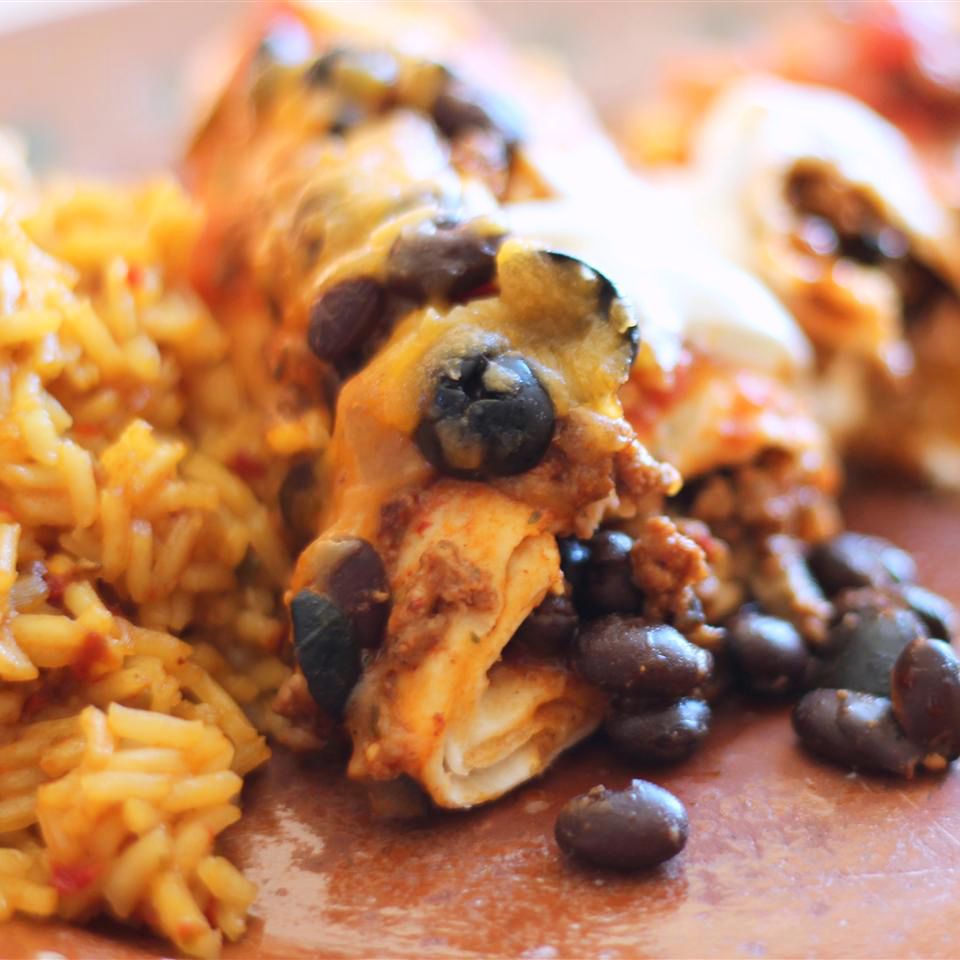 close up view of Beef Enchiladas with black beans and rice on a plate