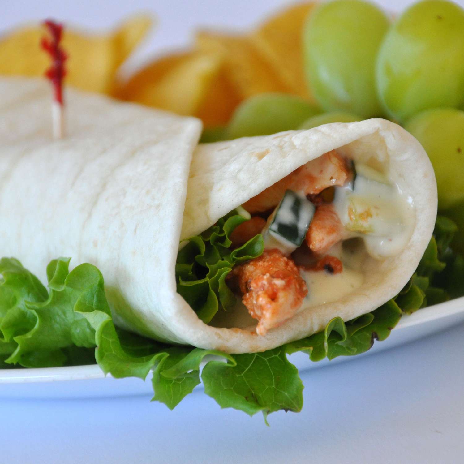 close up view of a Sweet and Spicy Chicken Wrap on a plate with lettuce and fruit