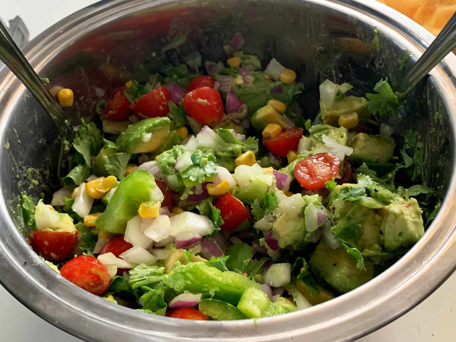 close up view of an Avocado Salad salad in a metal bowl; salad with avocados, tomatoes, peppers, corn, red onions and cilantro