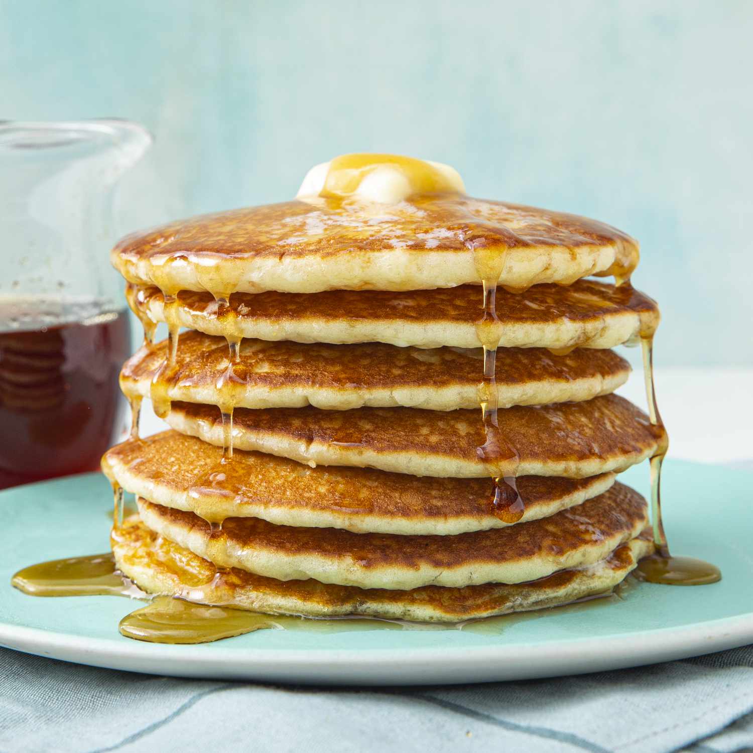 low angle looking at a stack of buttermilk pancakes topped with melty butter and syrup