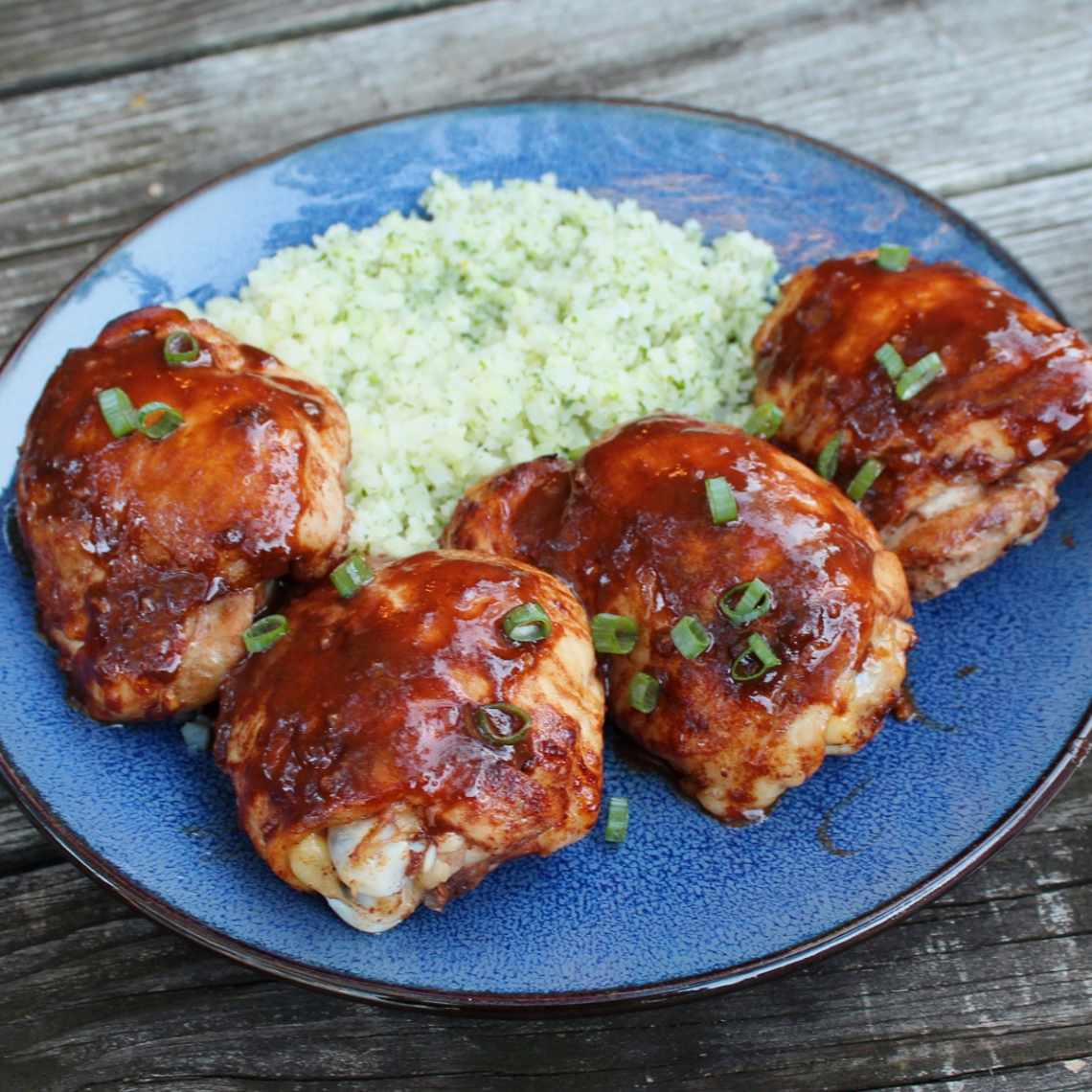 close up view of Asian Glazed Chicken Thighs on a blue plate with couscous