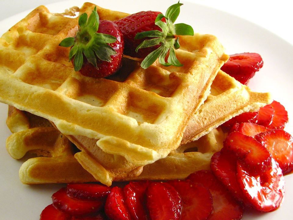 a stack of crisp-looking golden-brown waffles garnished with fresh sliced strawberries