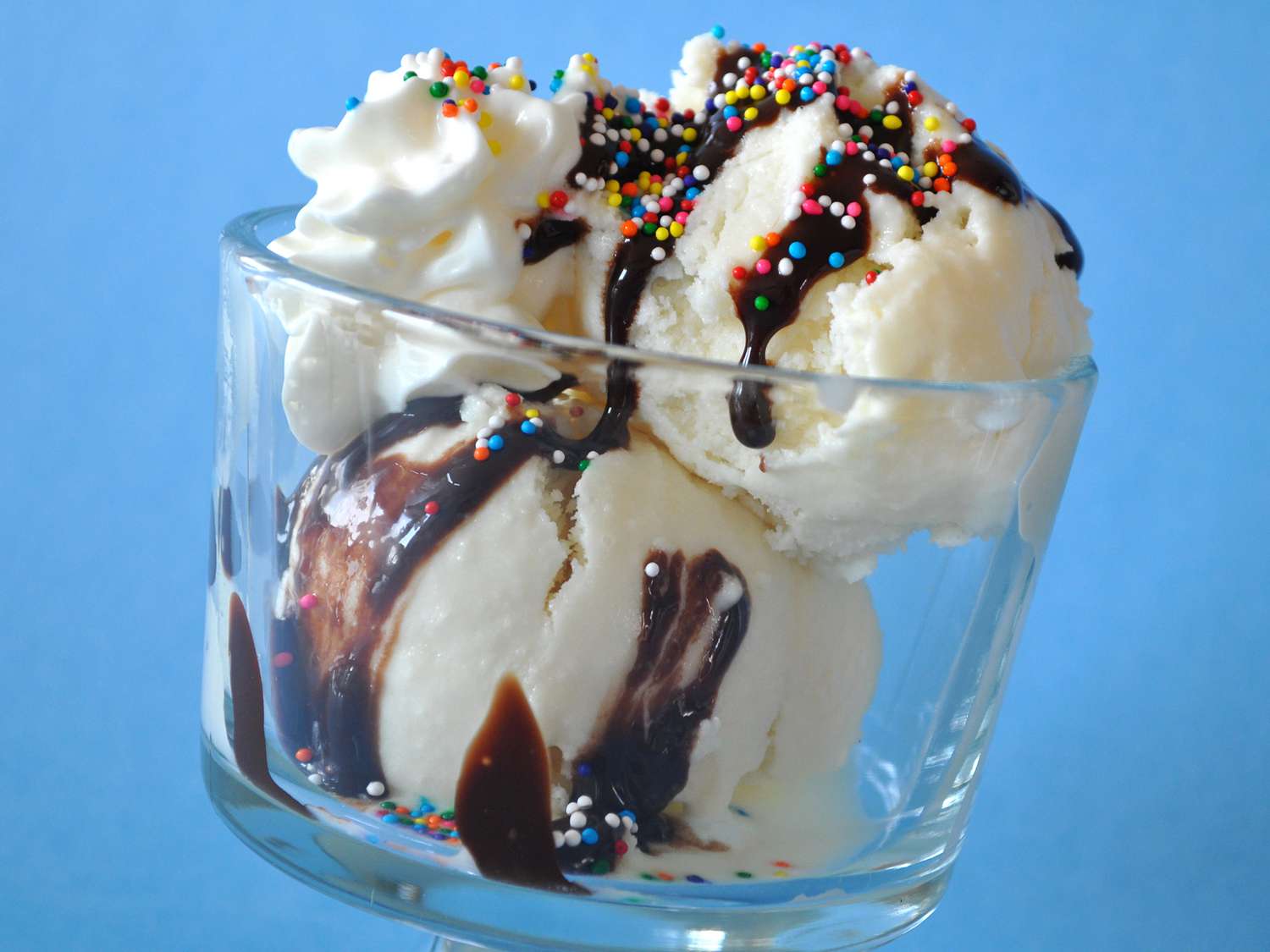 close up view of ice cream in a glass bowl topped with chocolate and rainbow sprinkles