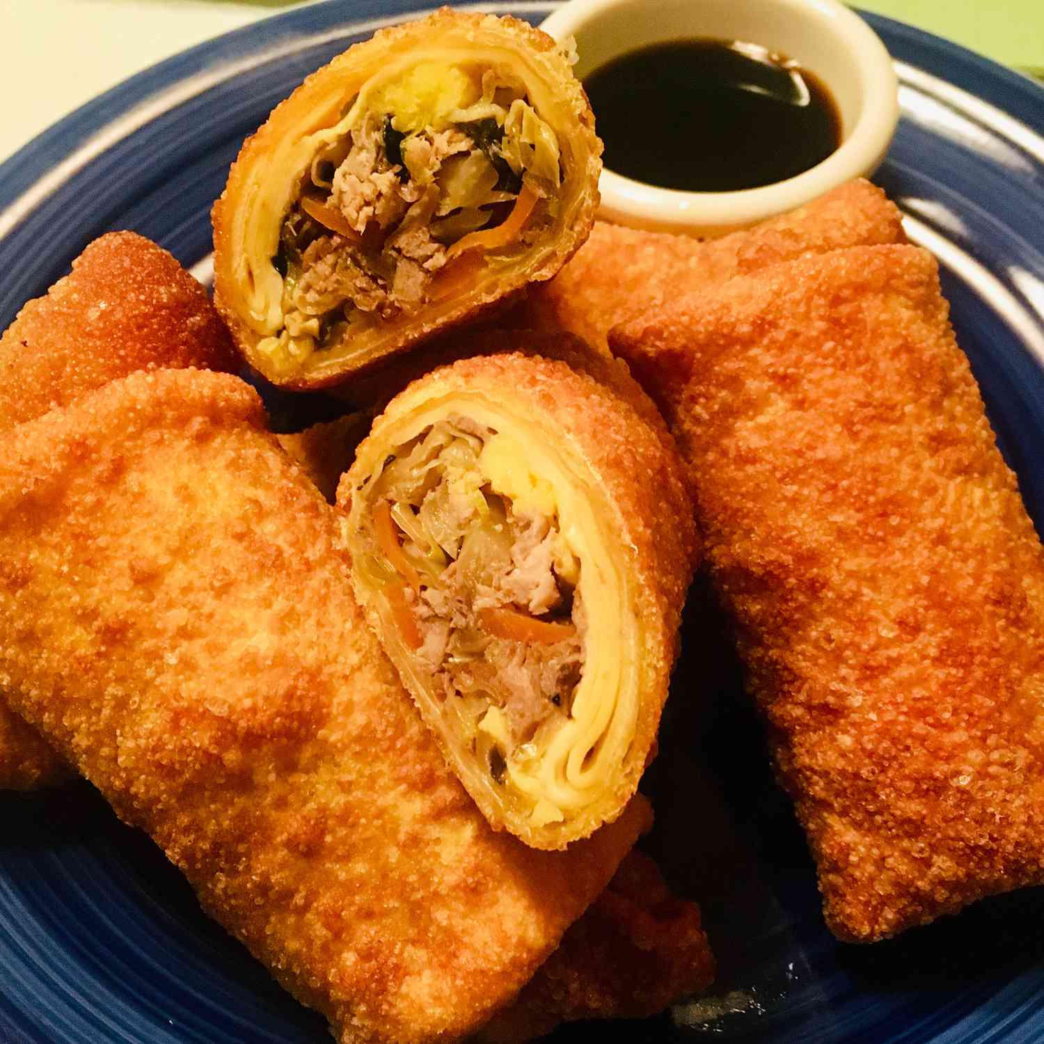 close up view of egg rolls with sauce on a blue plate