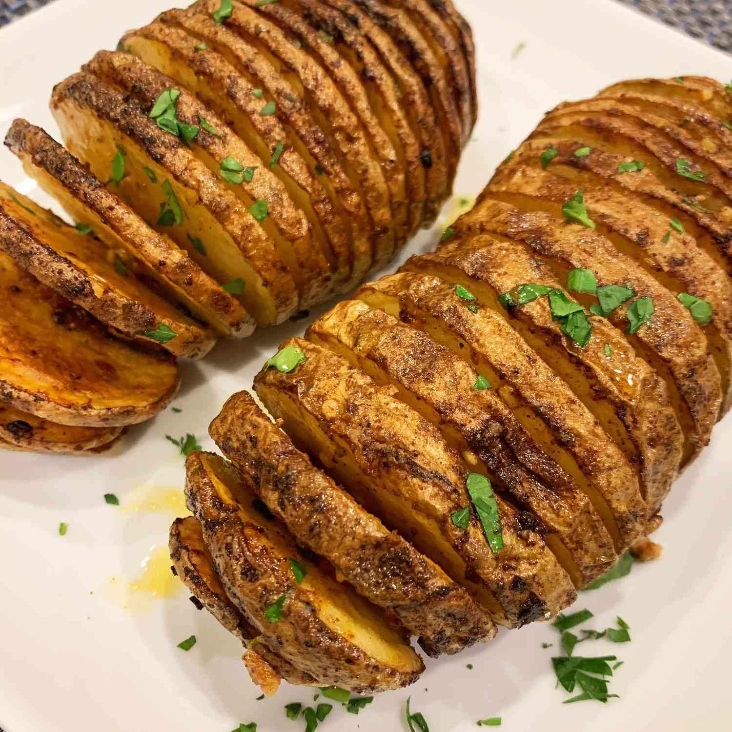 close up view of Air Fryer Hasselback Potatoes garnished with fresh herbs on a plate