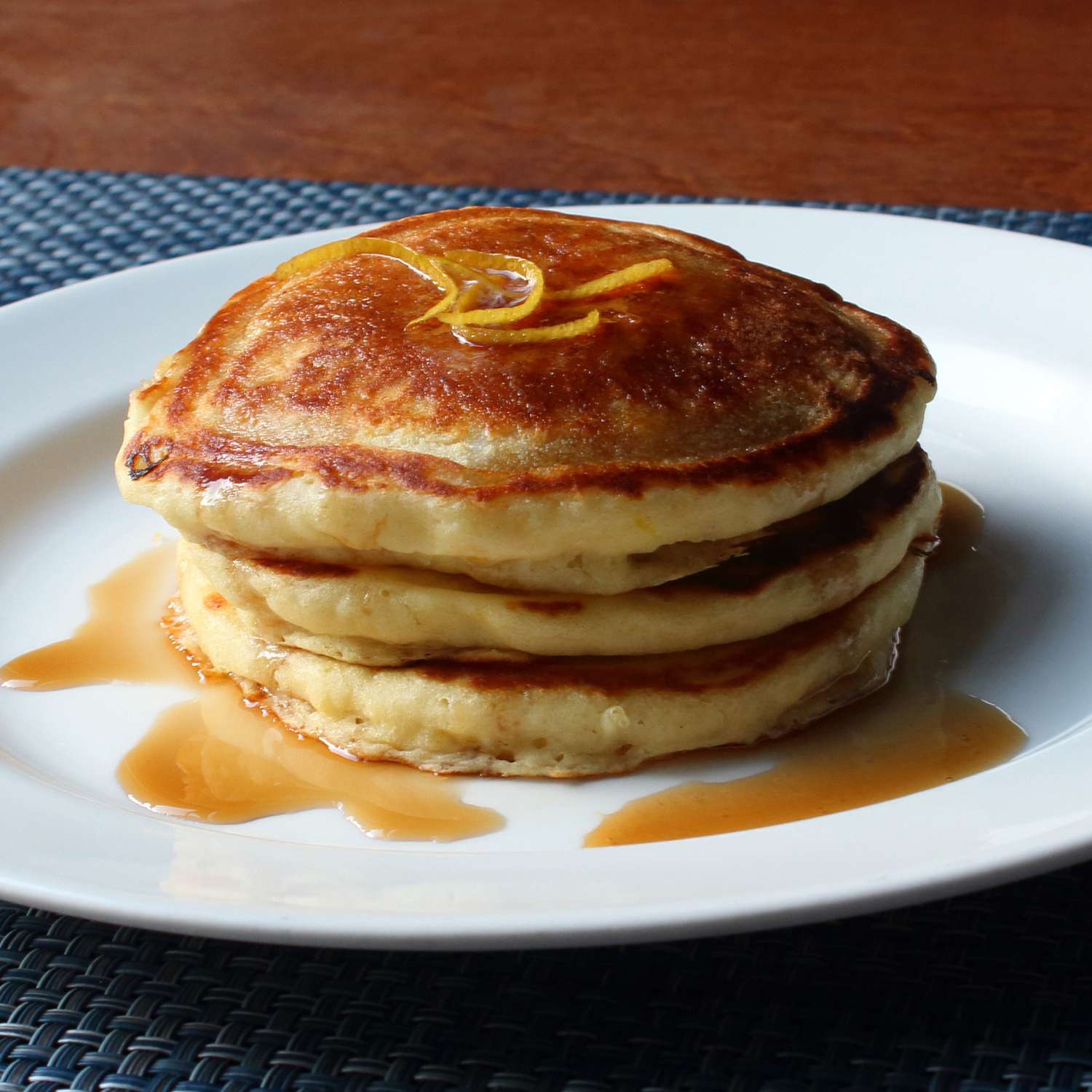 close up view of a stack of Lemon-Ricotta Pancakes with syrup and citrus zest on a white plate