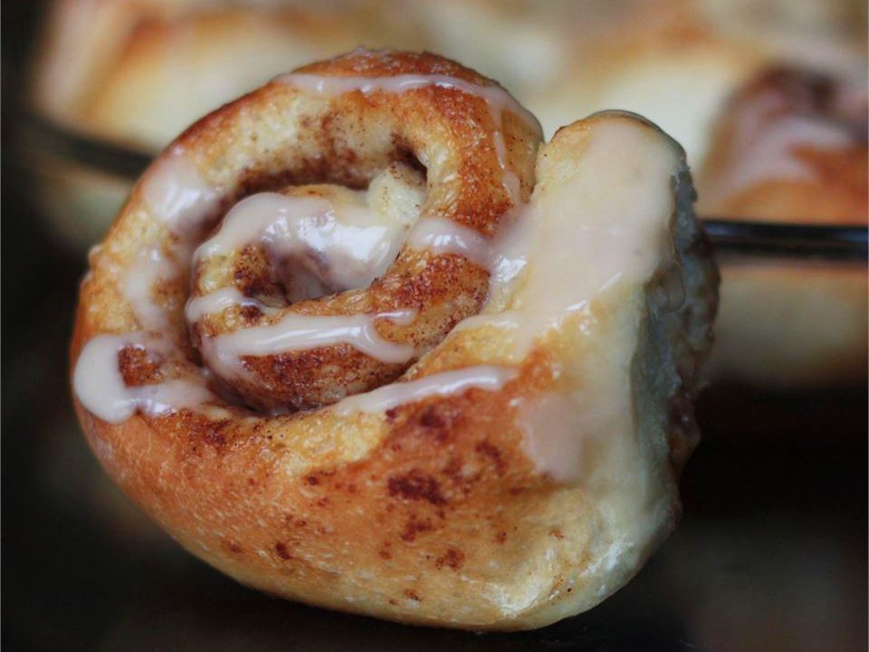 close up view of a cinnamon roll with a baking dish of cinnamon rolls in the background