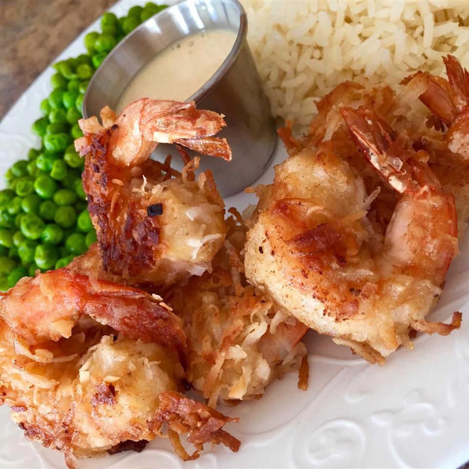 close up view of Coconut Shrimp on a plate with sauce, peas and rice on a white plate