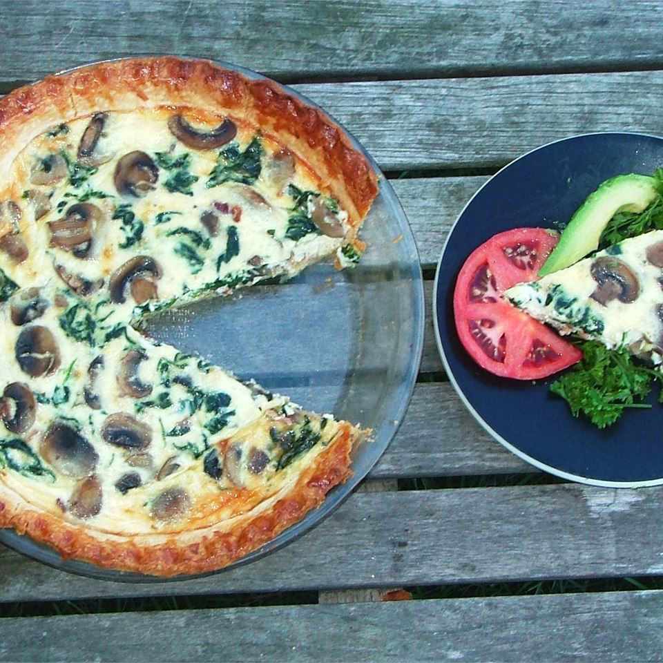overhead view of a quiche in a baking dish and a slice of quiche on a plate with a tomato slice, avocado and herbs