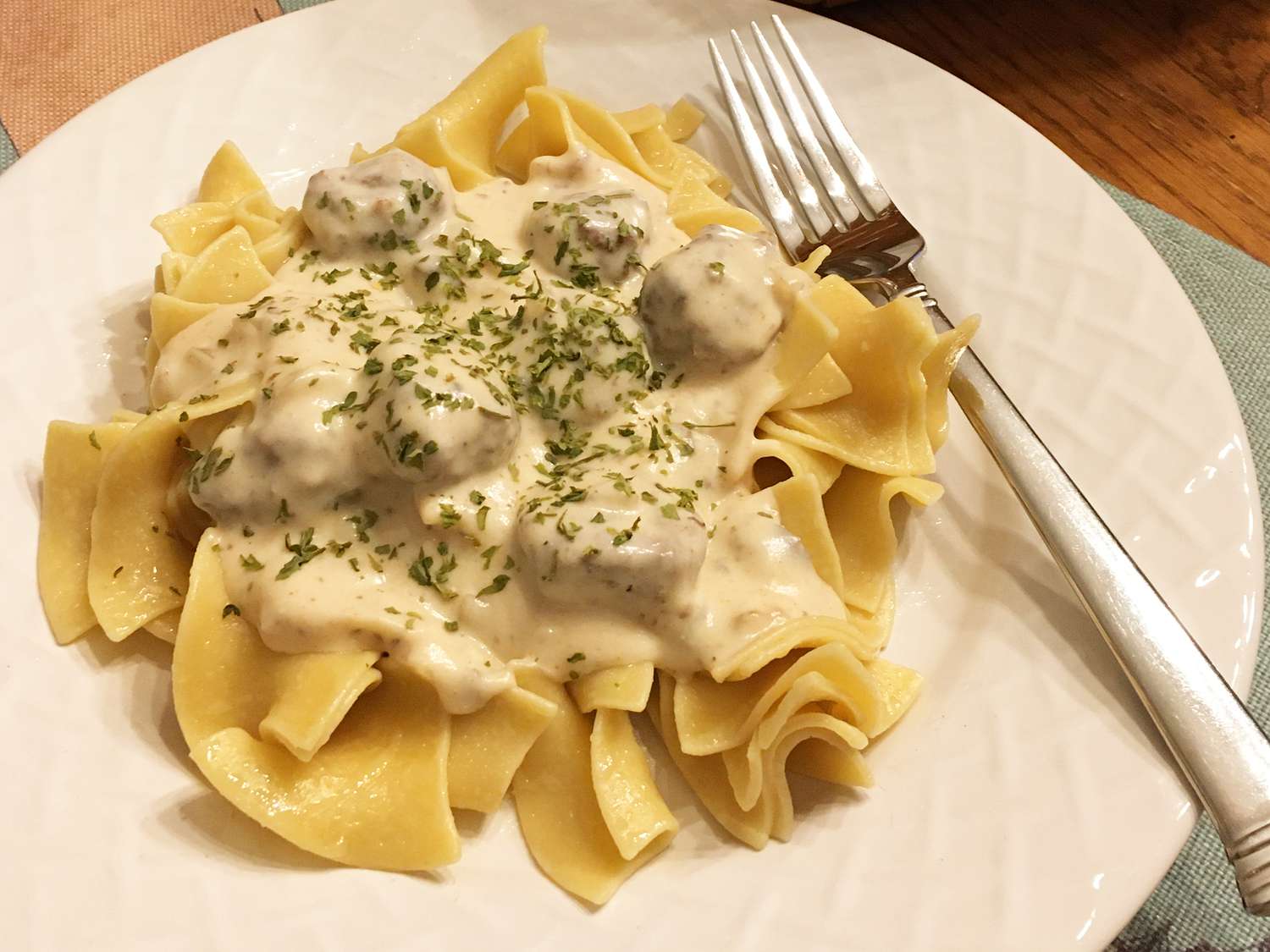 close up view of Meatball Stroganoff with sauce and herbs on a white plate with a fork