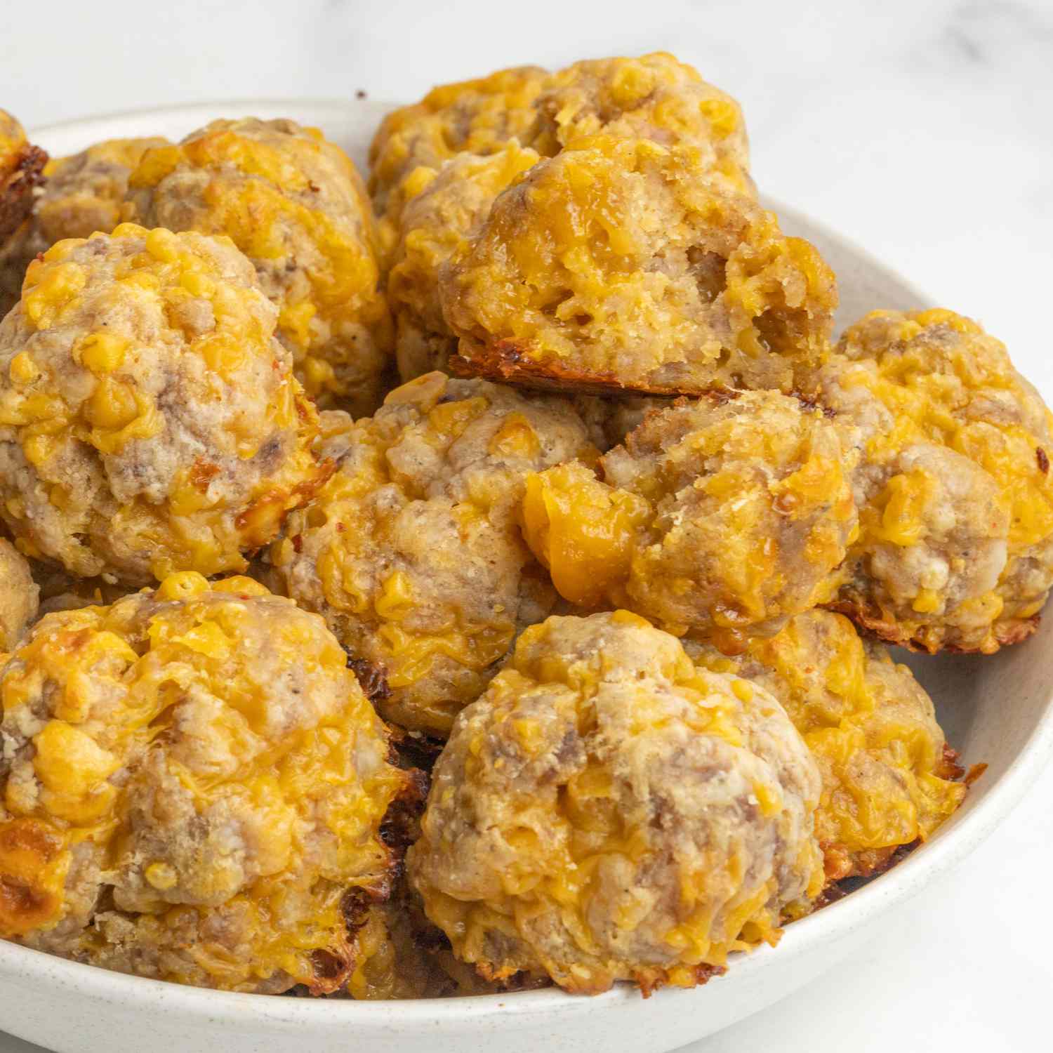 a close up view looking into a bowl full of bisquick sausage balls with one torn open.