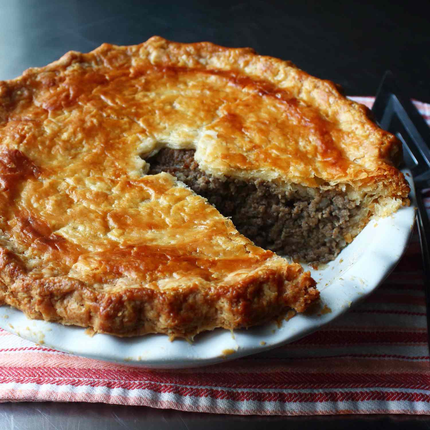 close up view of a Tourtiere in a pie pan, next to a pie server