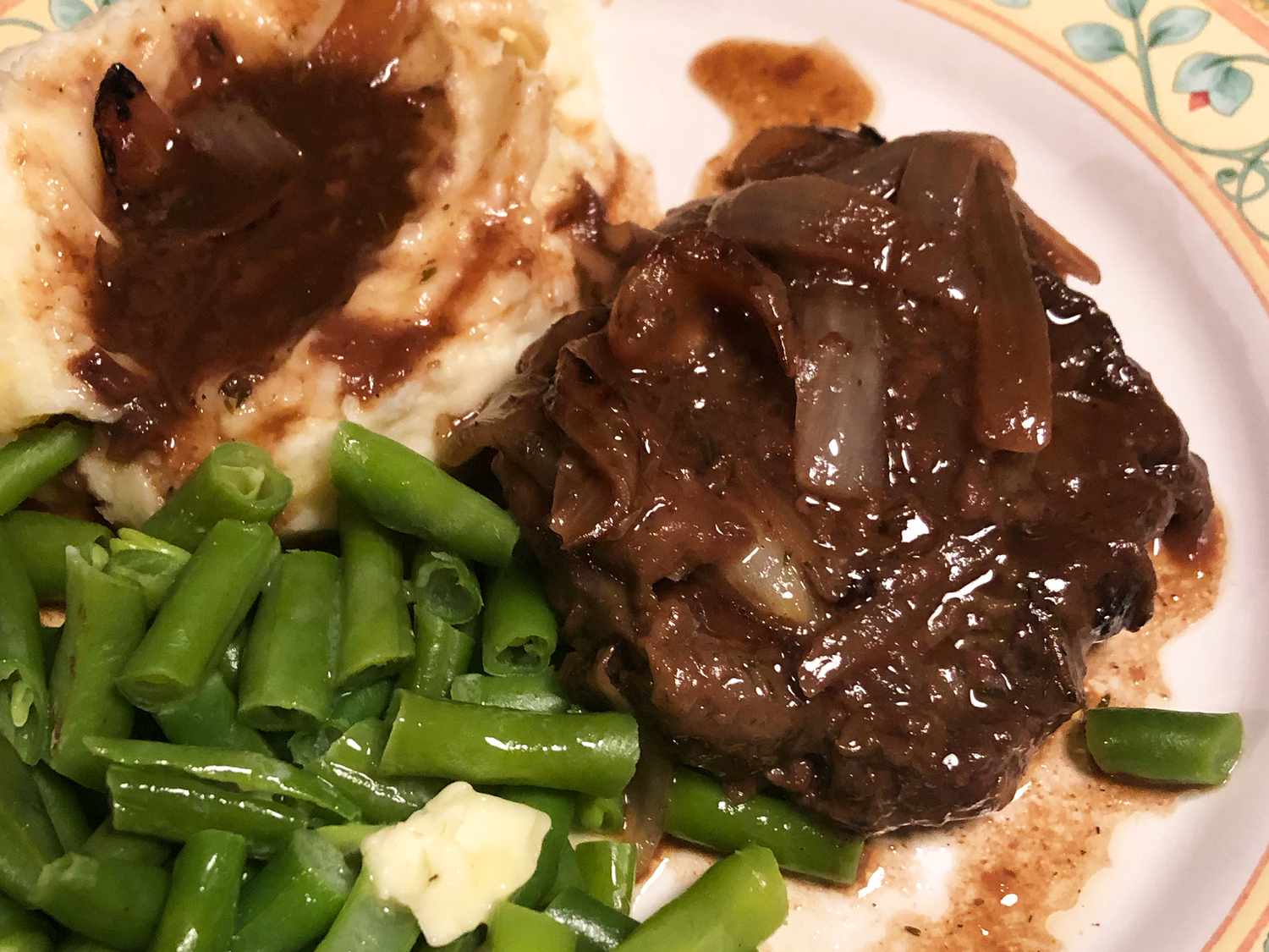 close up view of braised eye round steak served with green beans, mashed potatoes and gravy on a plate