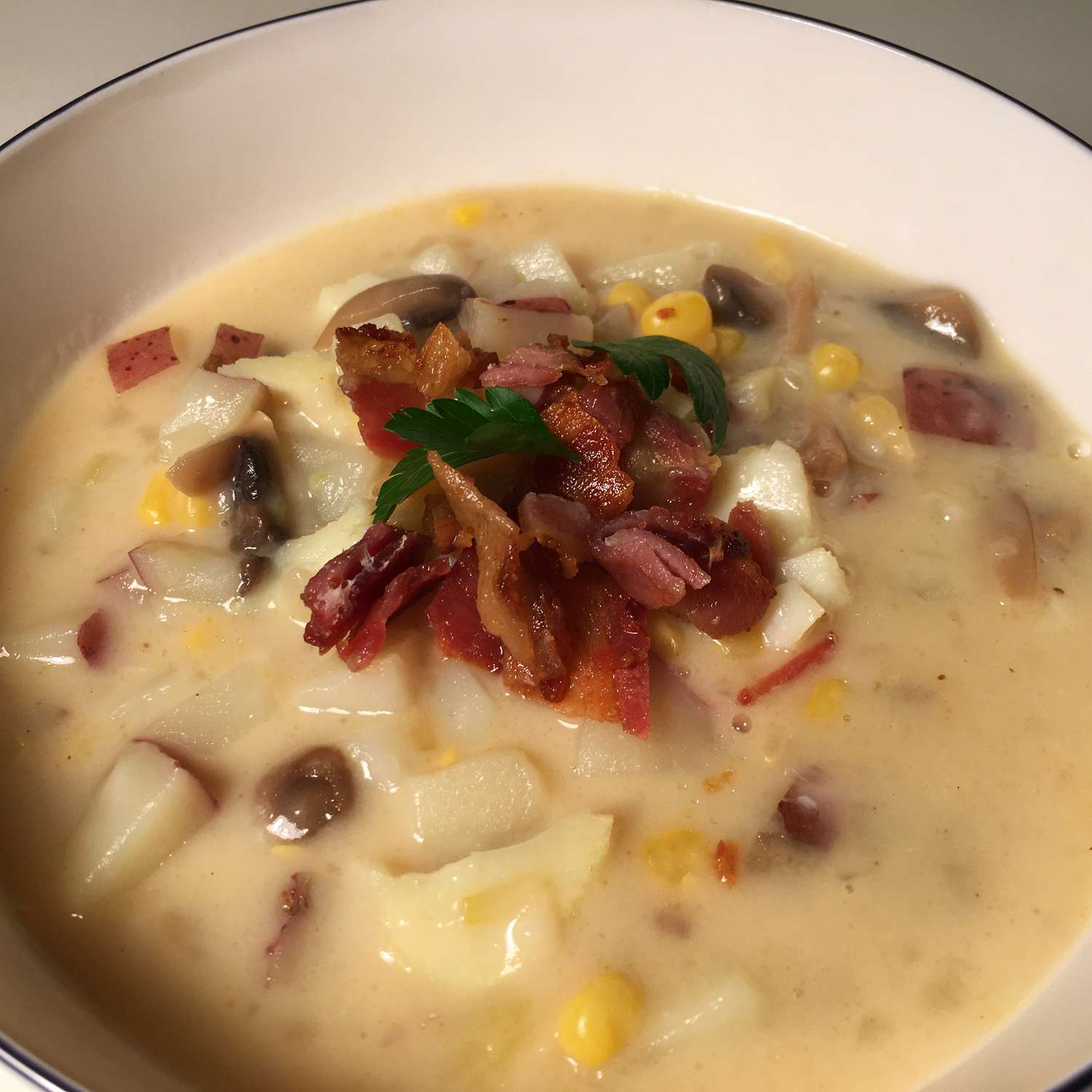 close up view of Fish Chowder garnished with bacon piece and fresh herbs in a bowl
