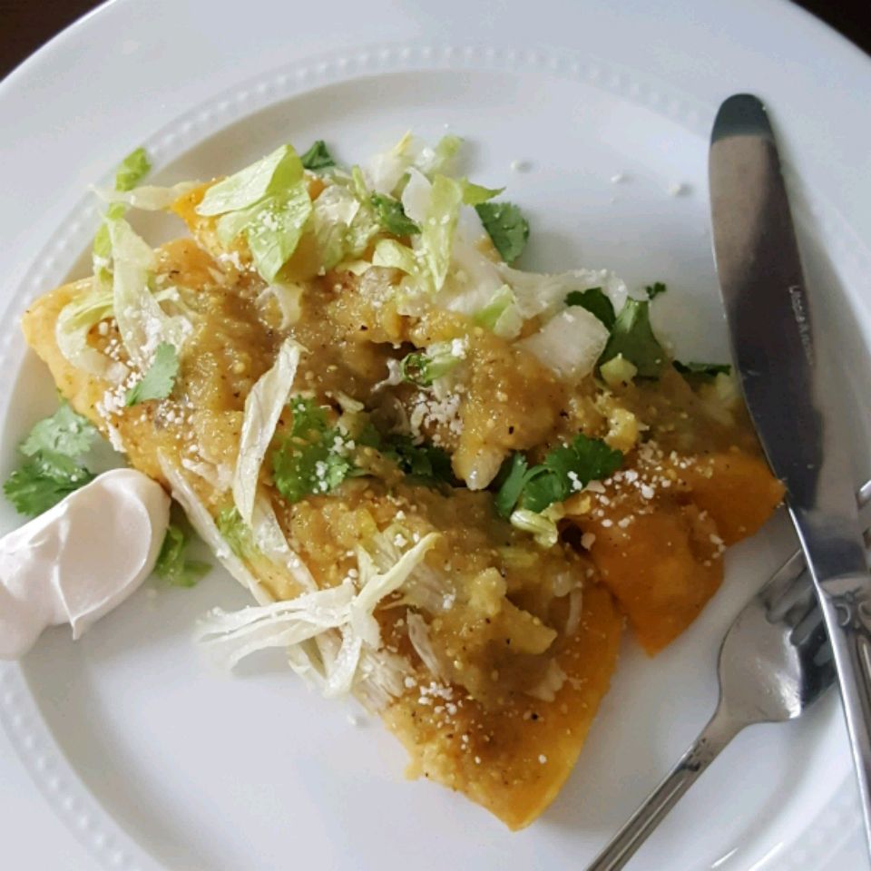 close up view of Enchiladas Verdes on a plate with sour cream a knife and fork