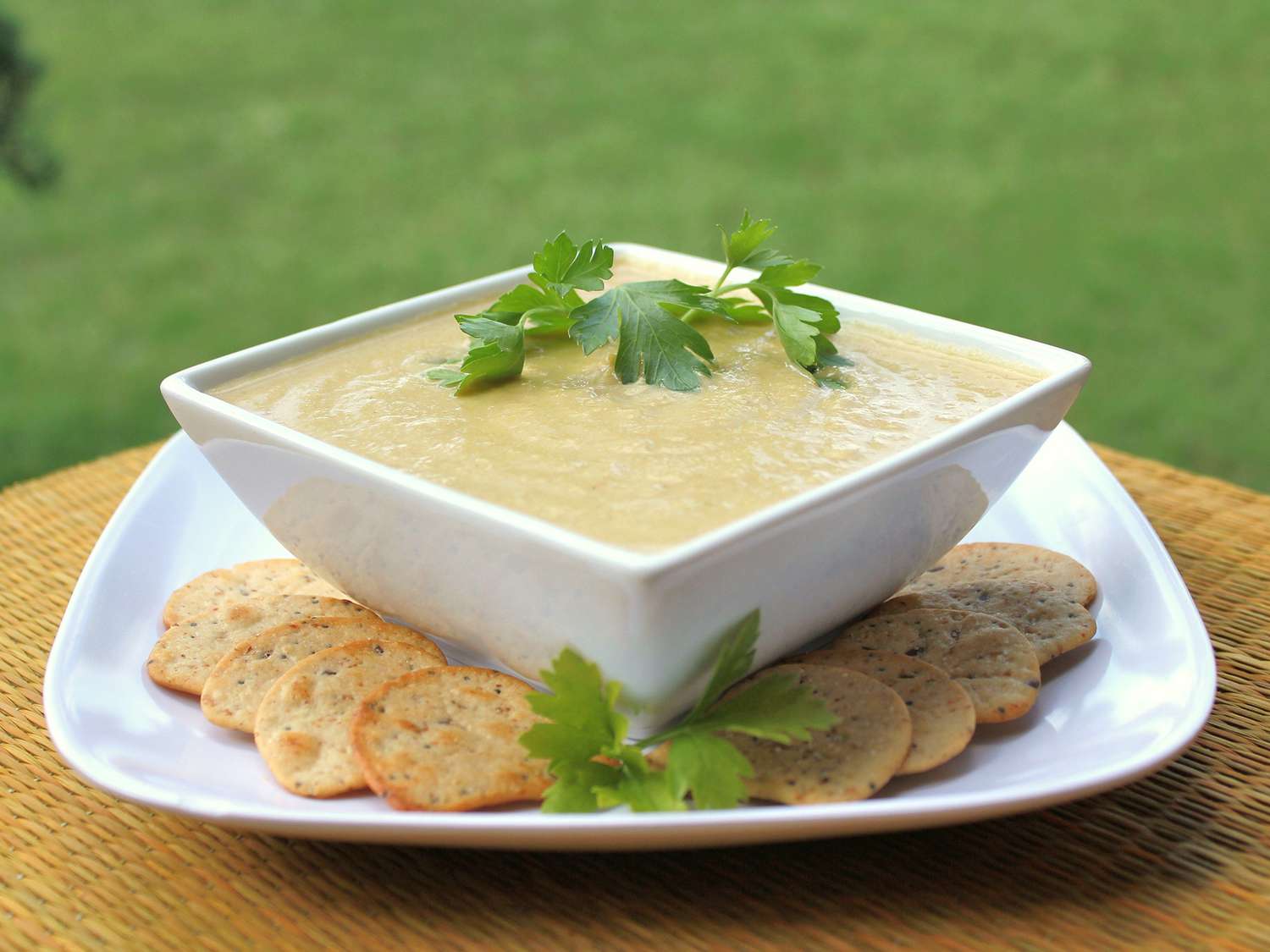 close up view of Low Carb Cauliflower Leek Soup garnished with fresh herbs in a square white bowl, served with crackers