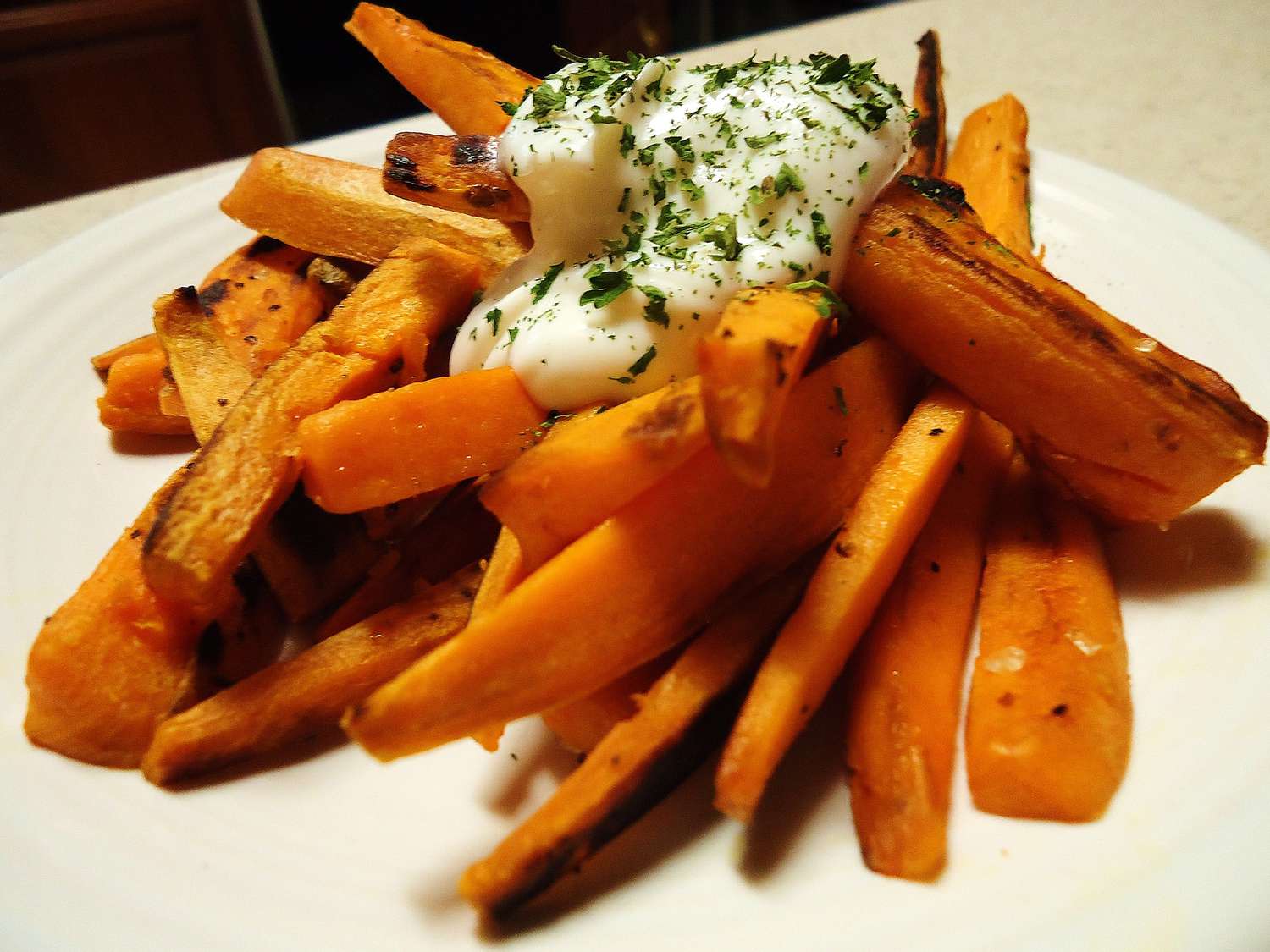 close up view of Fried Sweet Potatoes garnished with sauce and fresh herbs on a white plate