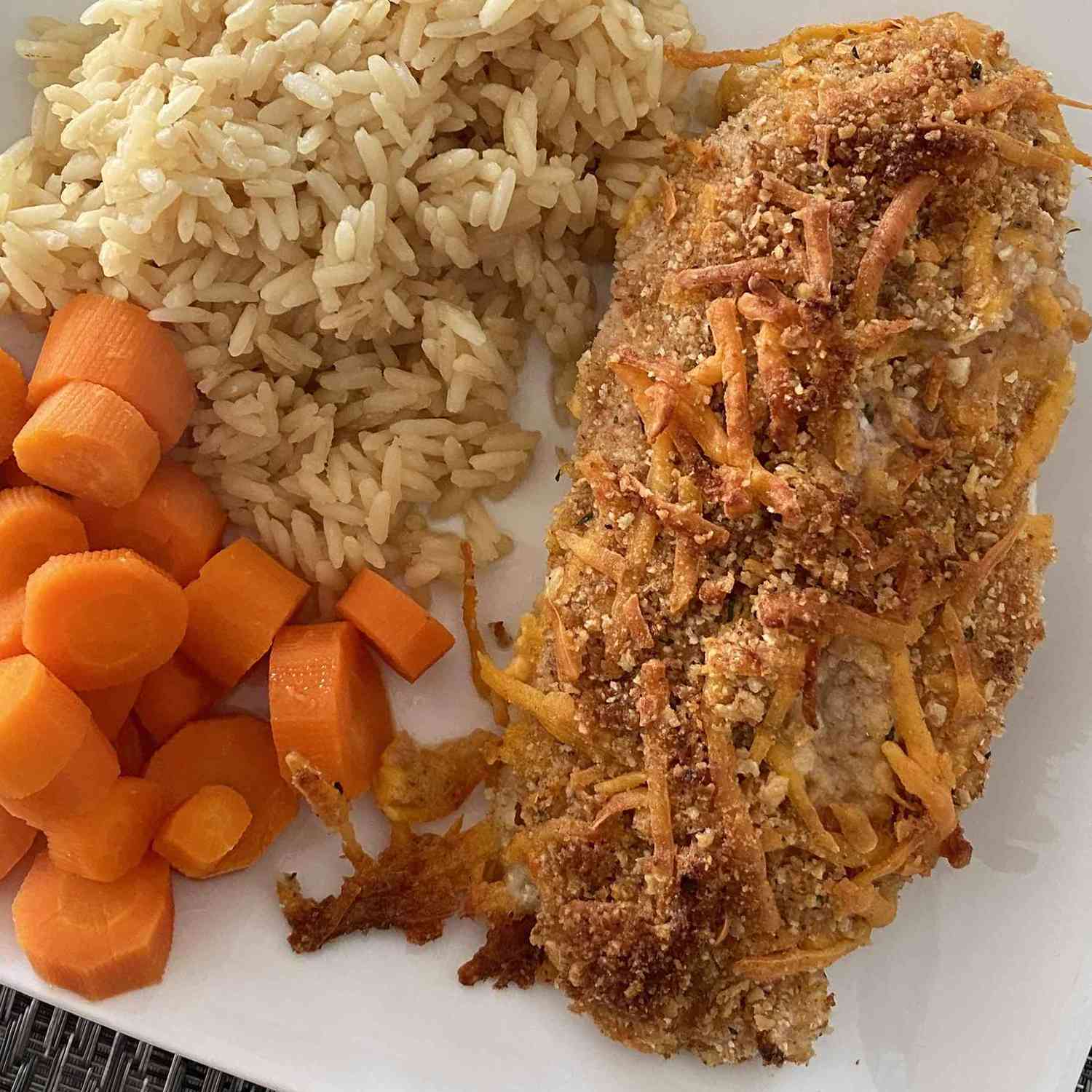 close up view of a Cheddar Baked Chicken fillet served with rice and carrots on a white plate