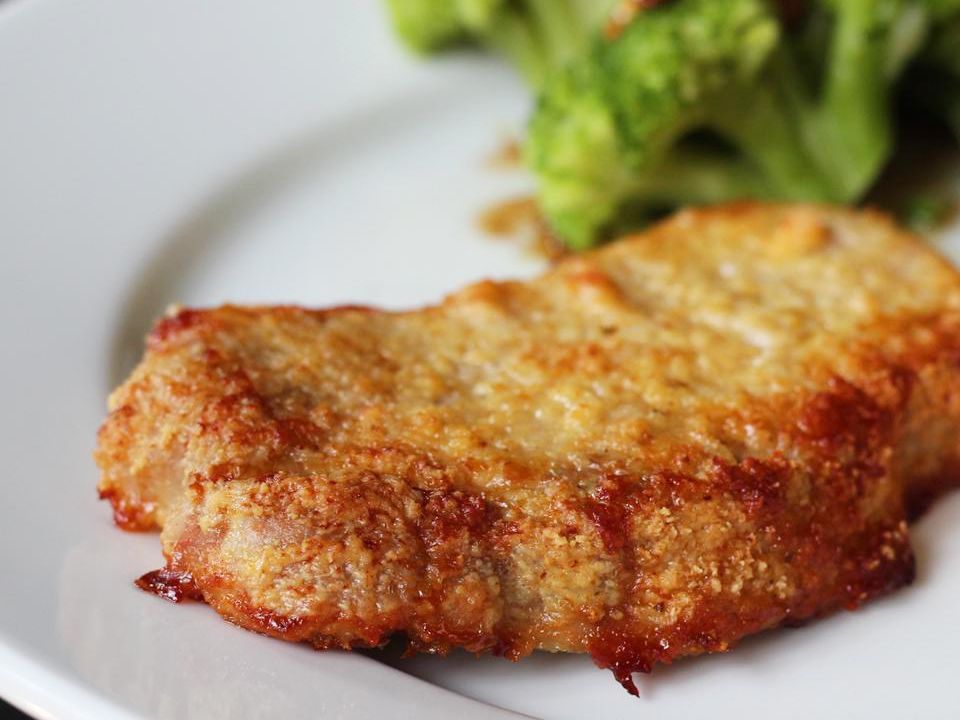 close up view of a Parmesan-Crusted Pork Chop with a salad on a white plate