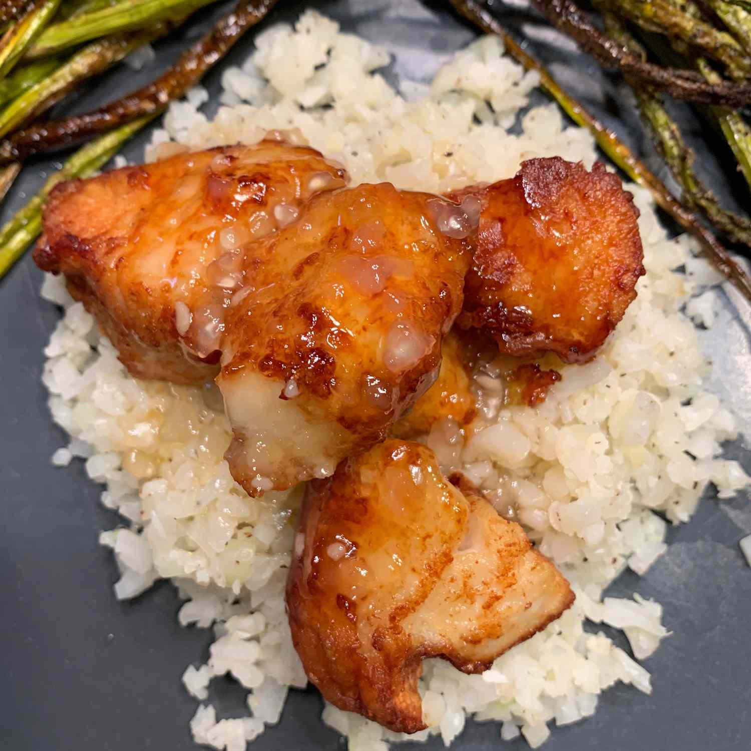 close up view of sesame chicken on top of white rice, with a side of asparagus on a blue plate