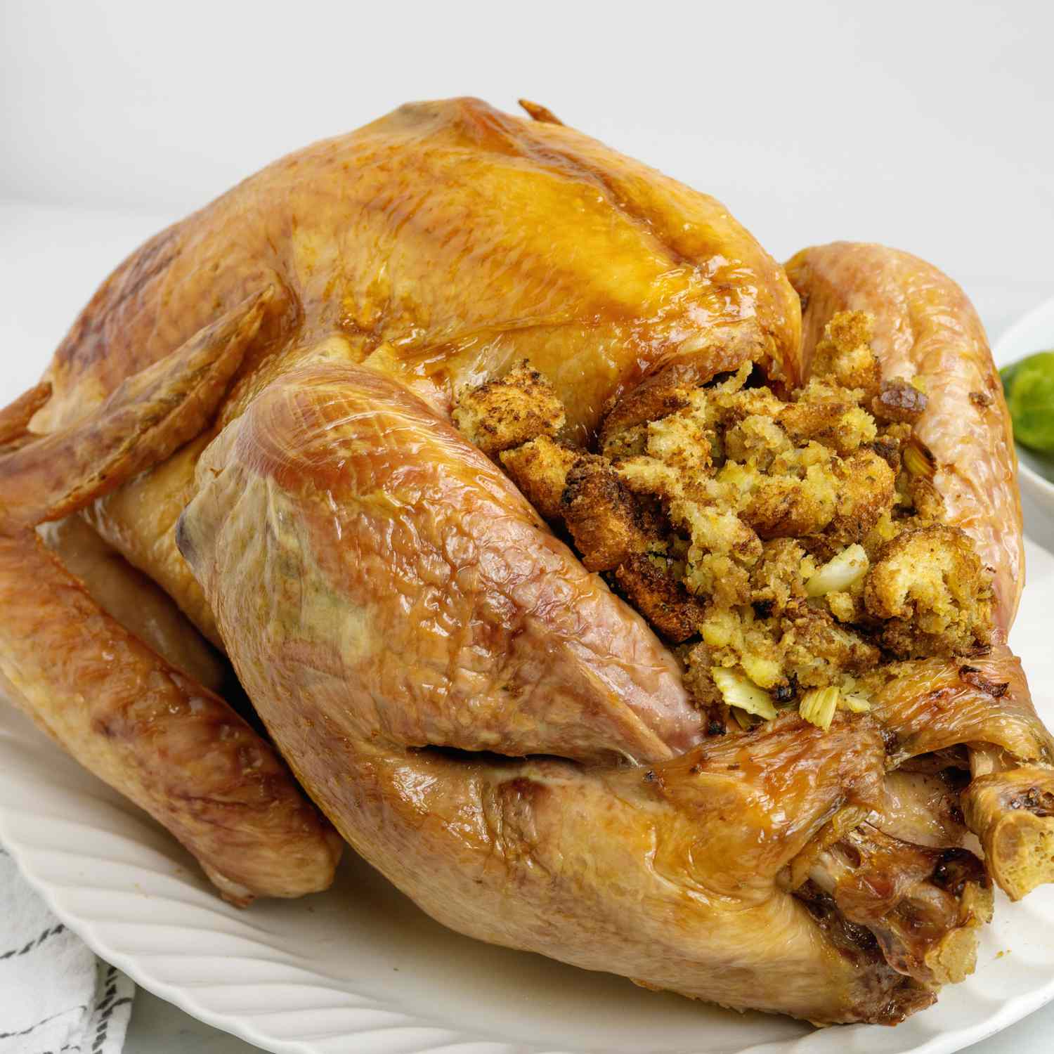 a mid level view of a golden brown turkey on a white oval platter, filled with traditional stuffing.