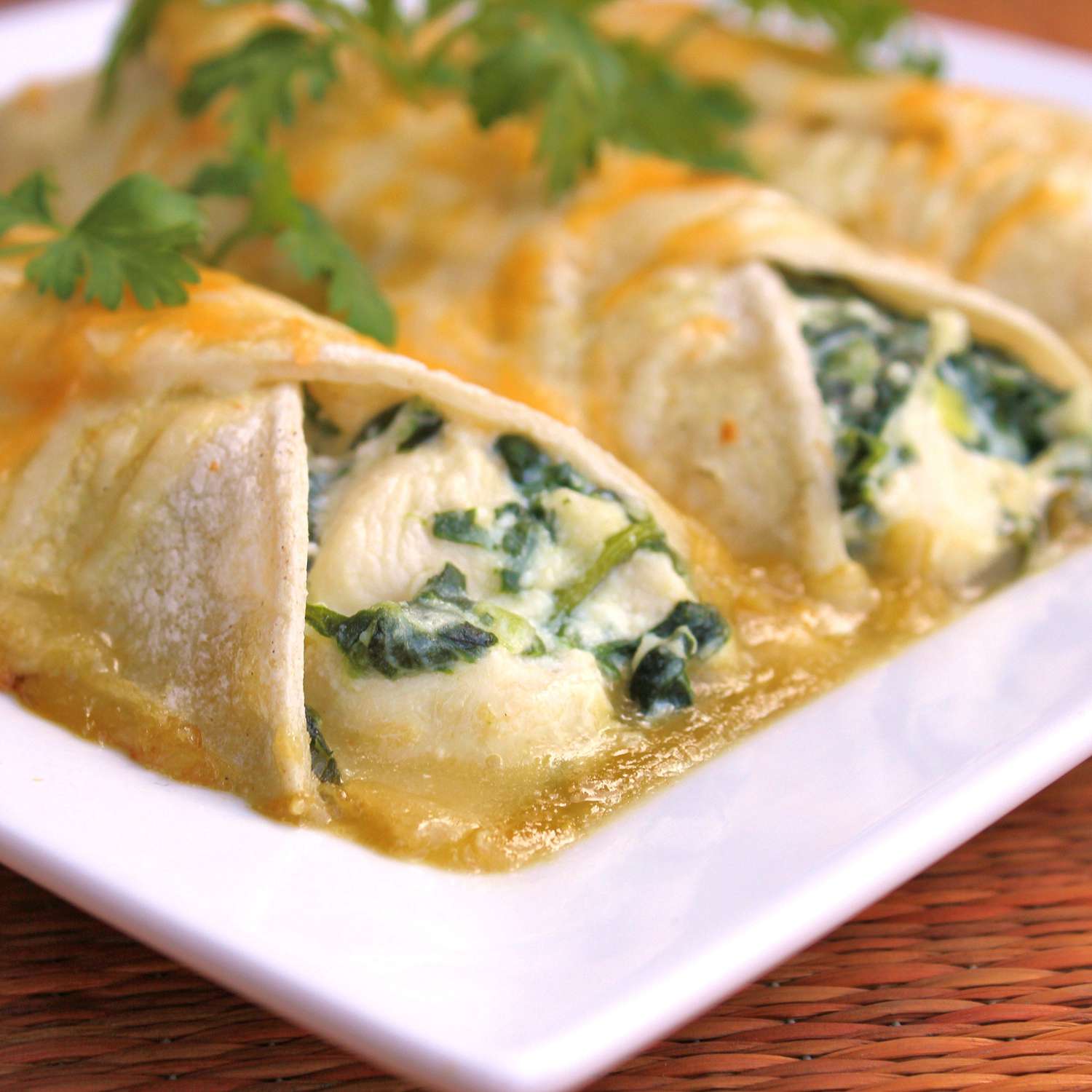 close up view Spinach Enchiladas garnished with fresh herbs on a white platter