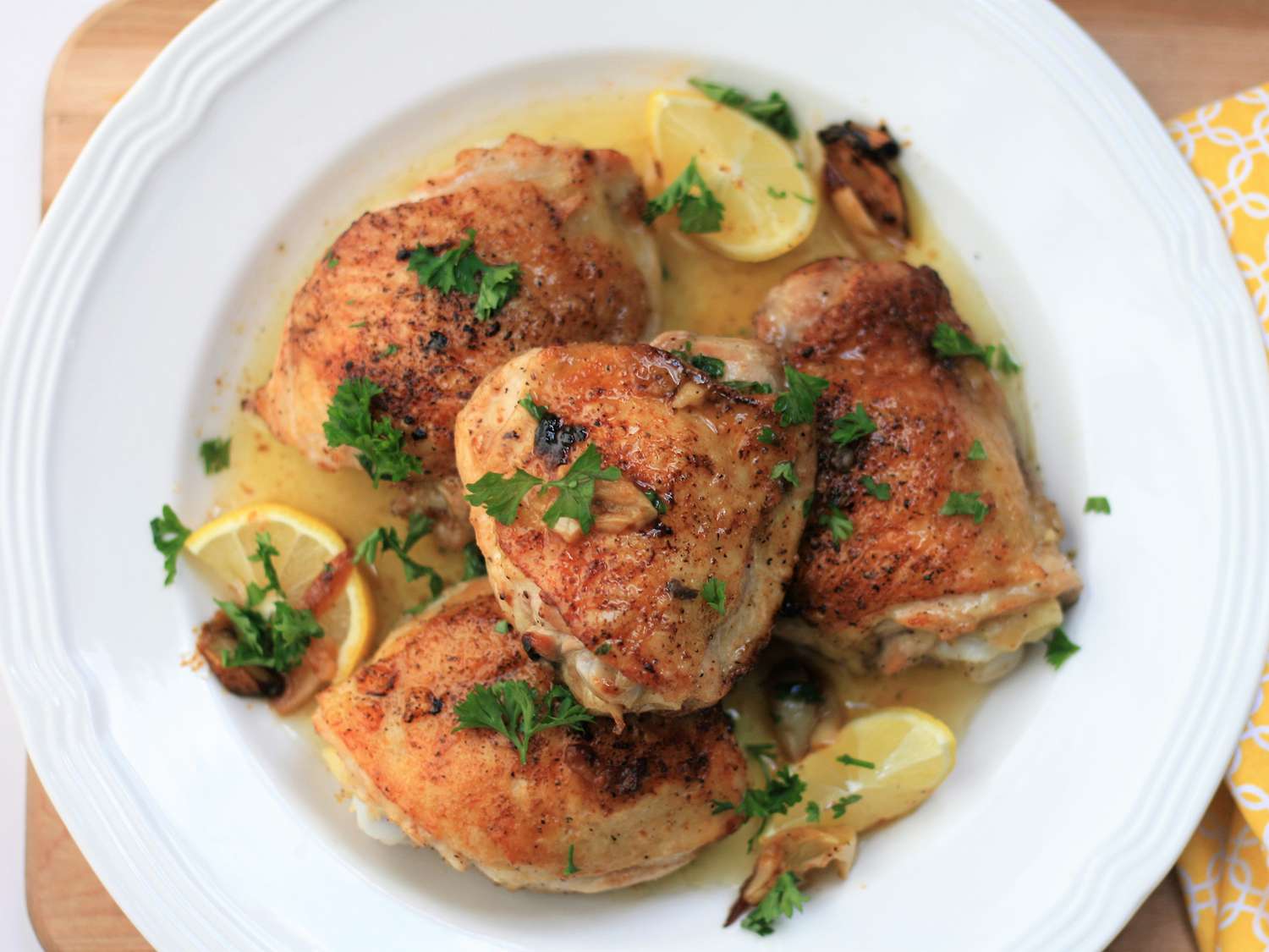 overhead view of Baked Lemon-Butter Chicken Thighs garnished with fresh herbs and lemon wedges in a white bowl