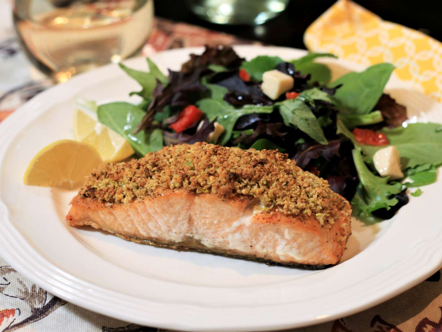 close up view of Pistachio-Crusted Salmon, served with salad and lemon wedges on a white plate