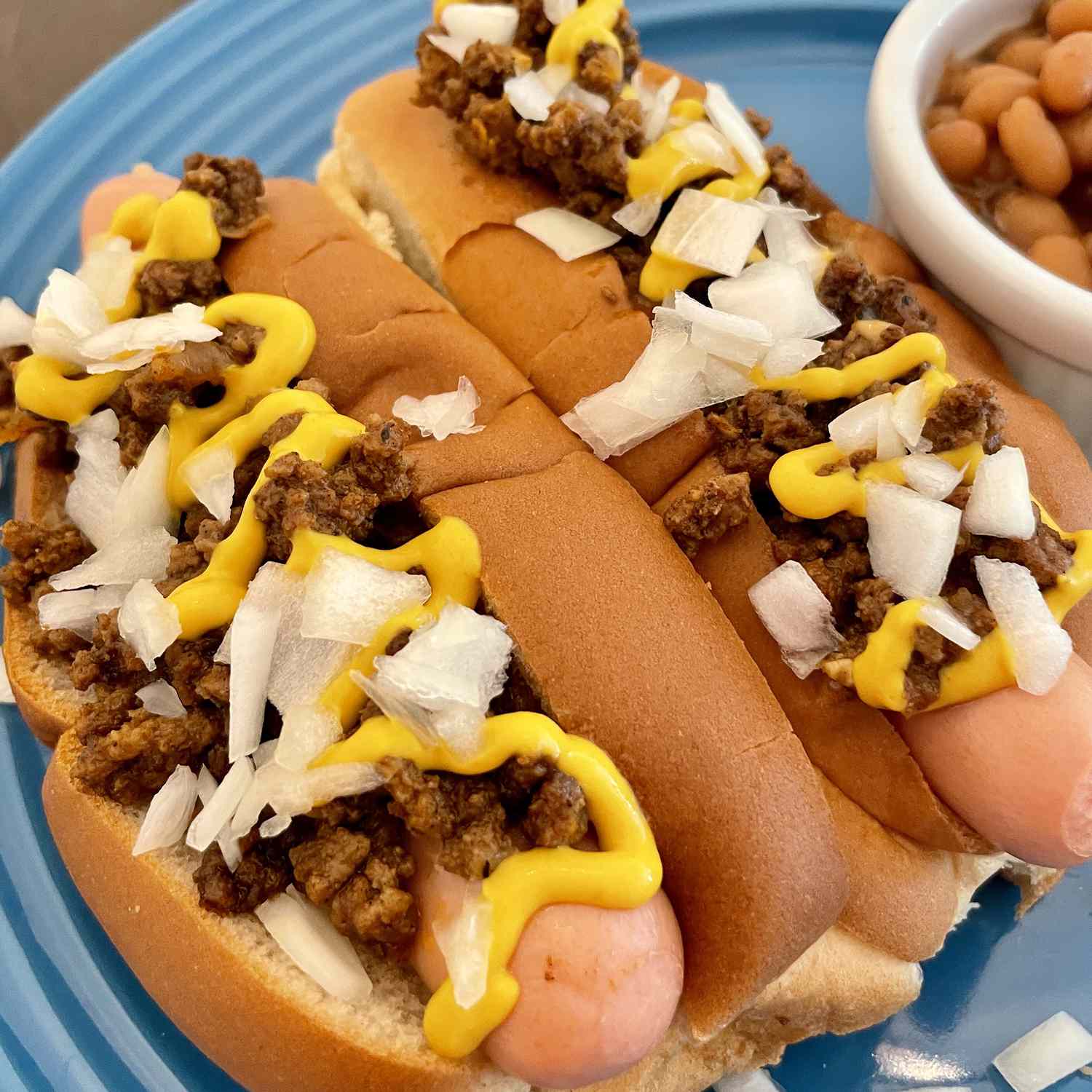 close up view of Coney Island Hot Dogs on a blue plate, with a side of beans