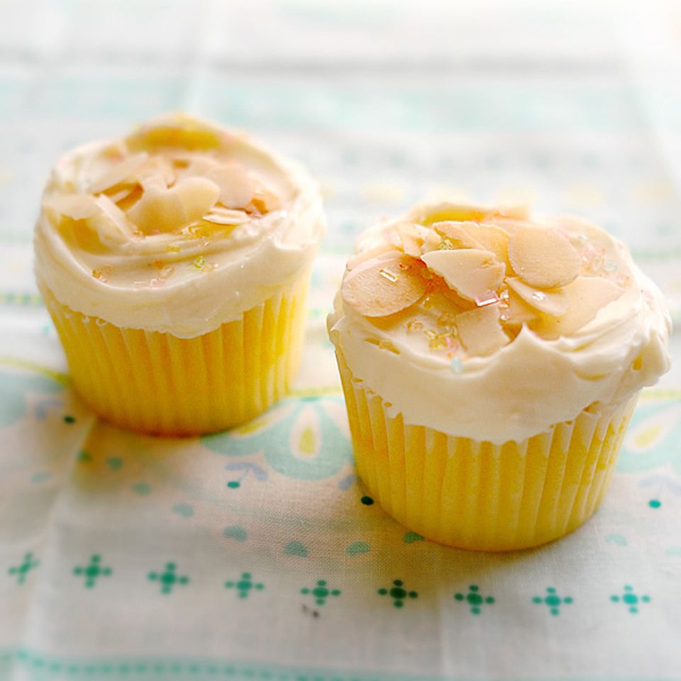 close up view of Lemon Cupcakes with white icing and almonds on top, on a blue and white table cloth