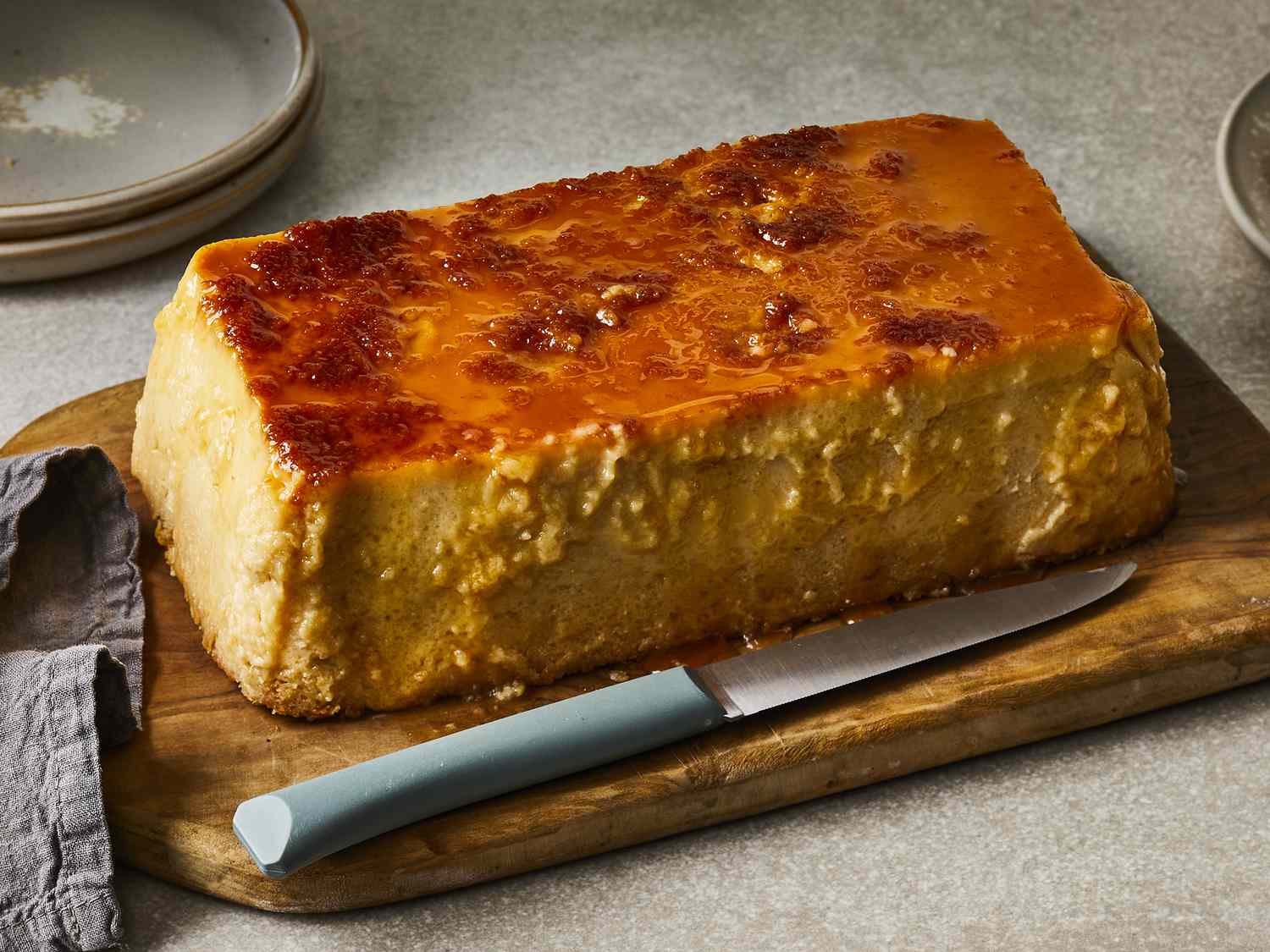 close up view of Budin (Puerto Rican Bread Pudding) on a wooden cutting board with a knife