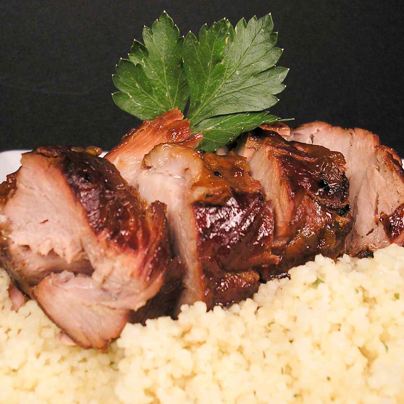 close up view of sliced Teriyaki Pork Tenderloin garnished with fresh herbs on top of couscous