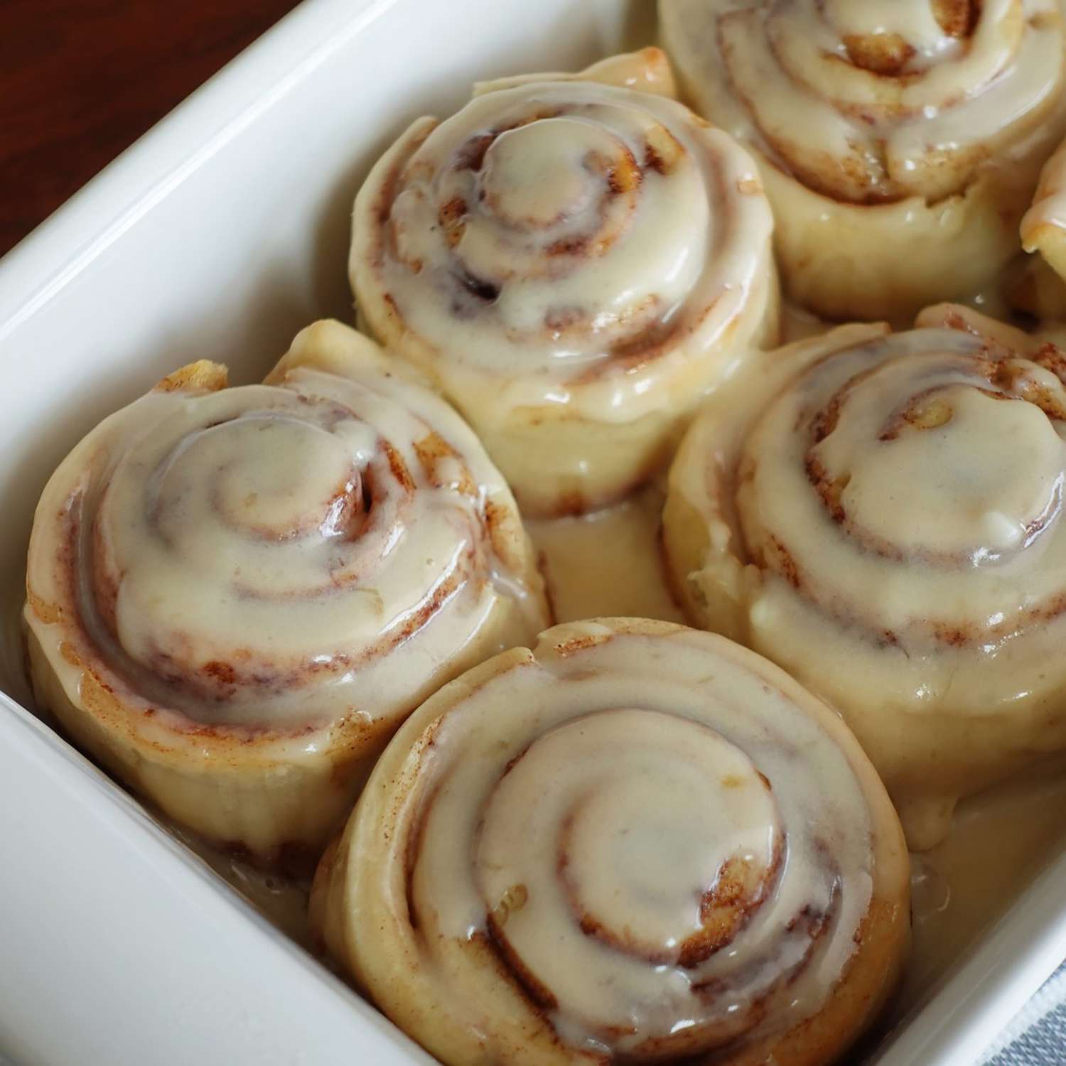 A baking dish full of large cinnamon rolls coated with icing.