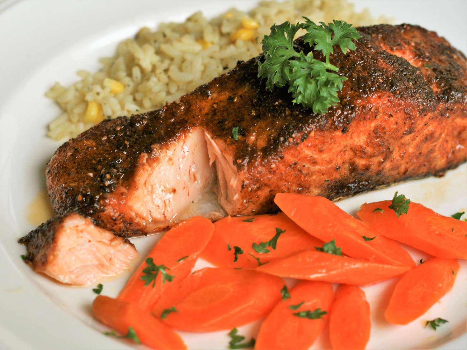 close up view of Cajun Air Fryer Salmon garnished with fresh herbs, served with carrots and rice on a plate