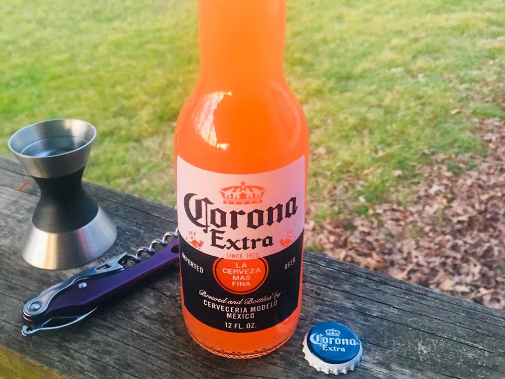 close up view of a Corona Sunrise in a corona bottle, a bottle opener, and a jigger