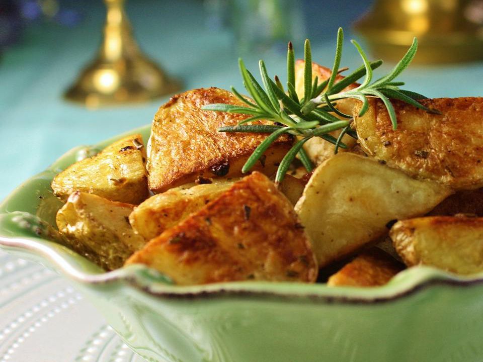 close up view of Amazing Oven Roasted Potatoes garnished with rosemary in a green bowl