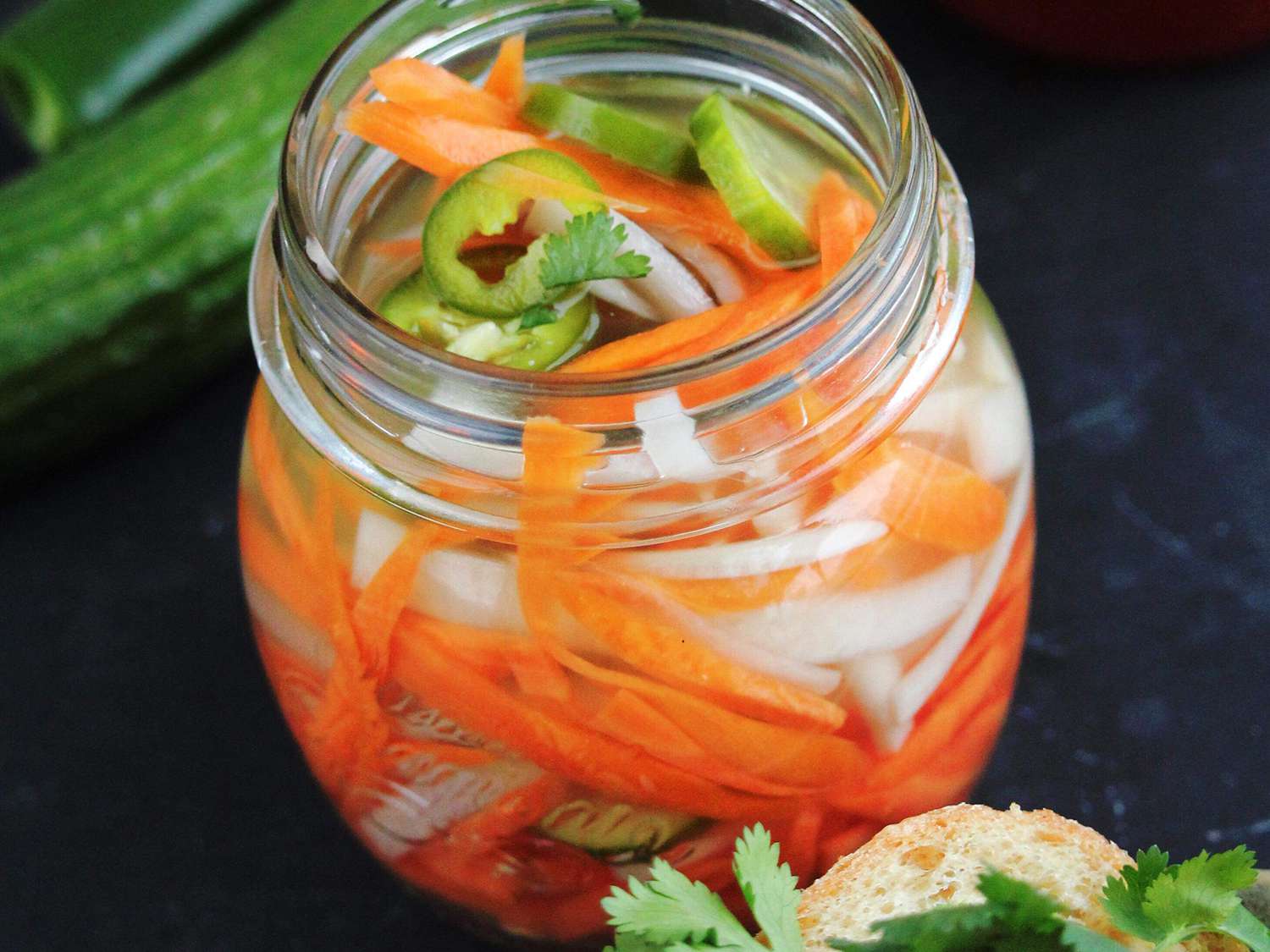close up view of Spicy Vietnamese Quick Pickled Vegetables in a jar, with a cucumber in the background