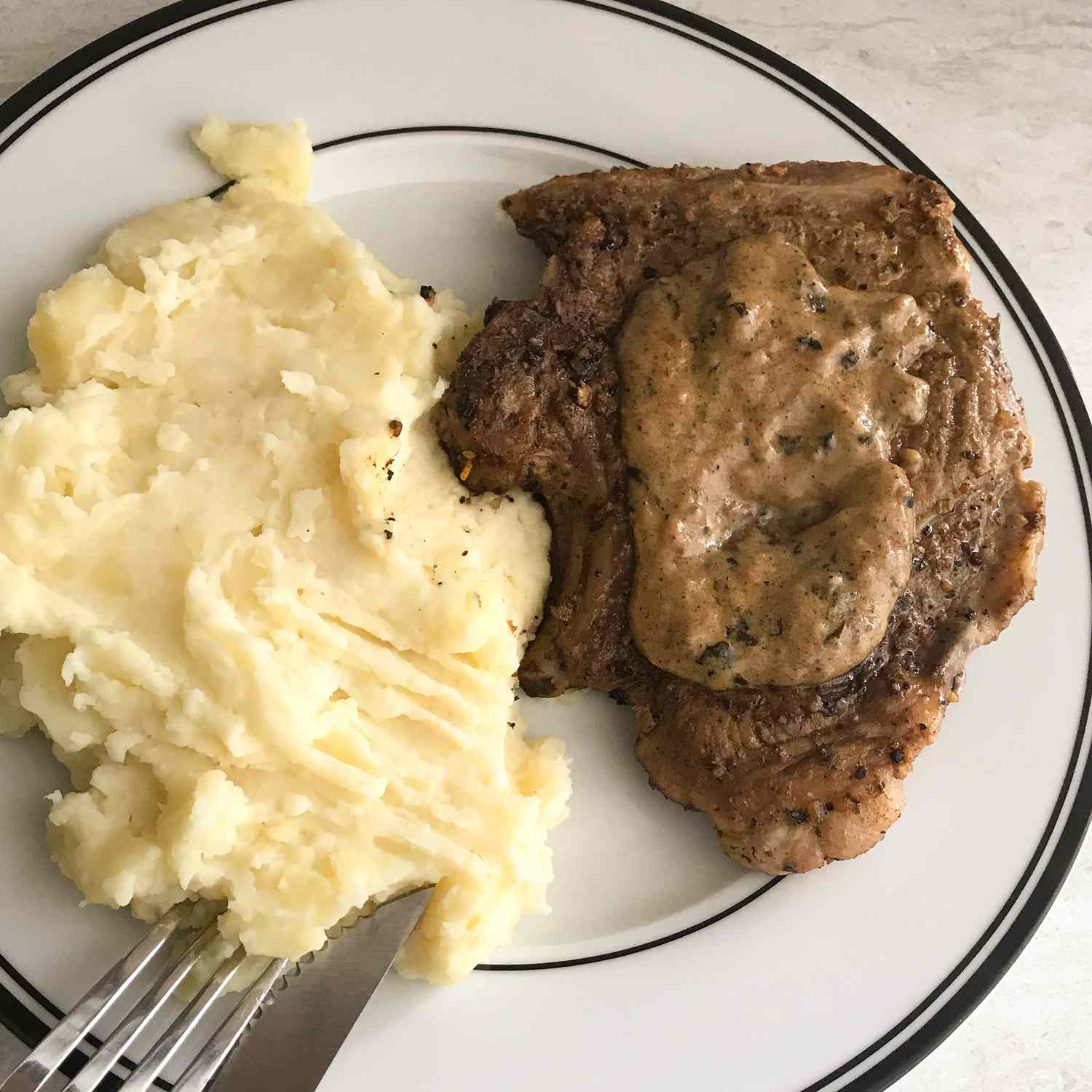close up view of Creamy Herbed Pork Chops served with mashed potatoes on a white plate