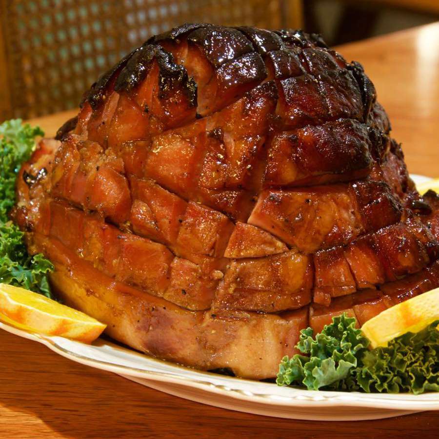 close up view of Honey-Glazed Ham on a platter with greens and orange slices on a platter