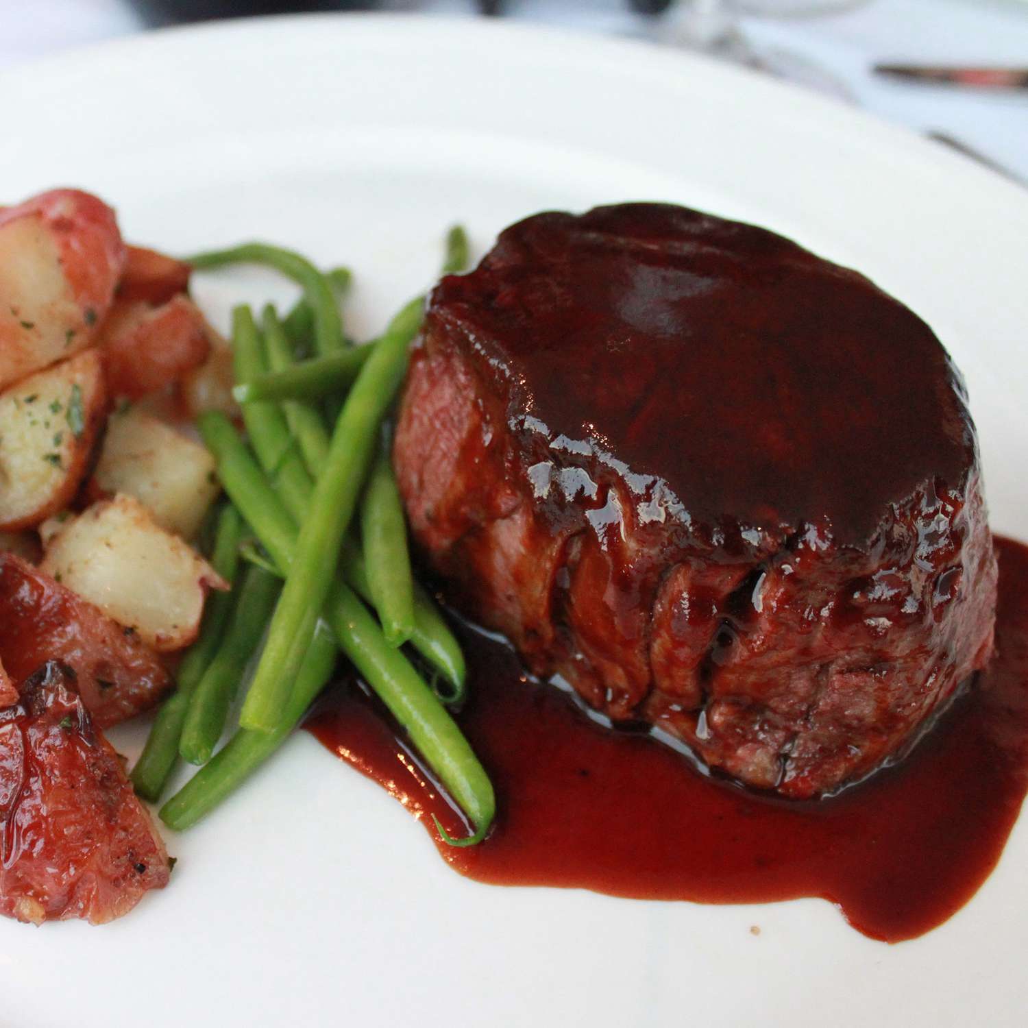 close up view of Filet Mignon with Rich Balsamic Glaze, served with red potatoes and green beans on a white plate