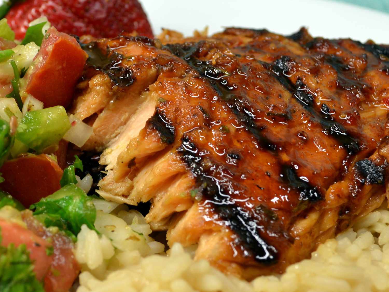close up view of a Hoisin-Glazed Salmon fillet on rice, with salad and a strawberry
