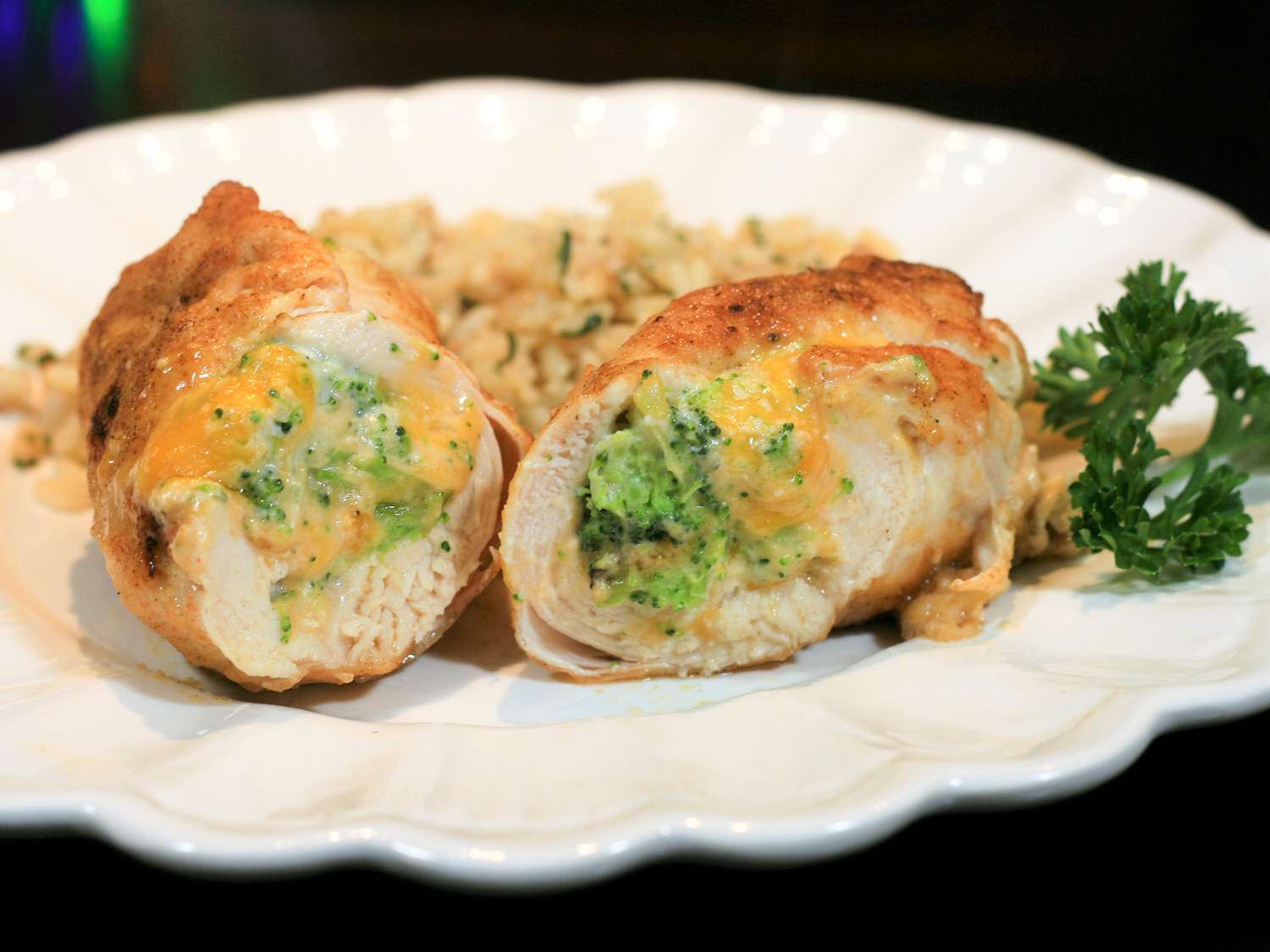 close up view of a sliced Broccoli Cheese Stuffed Chicken served on a white plate with grains and fresh herbs