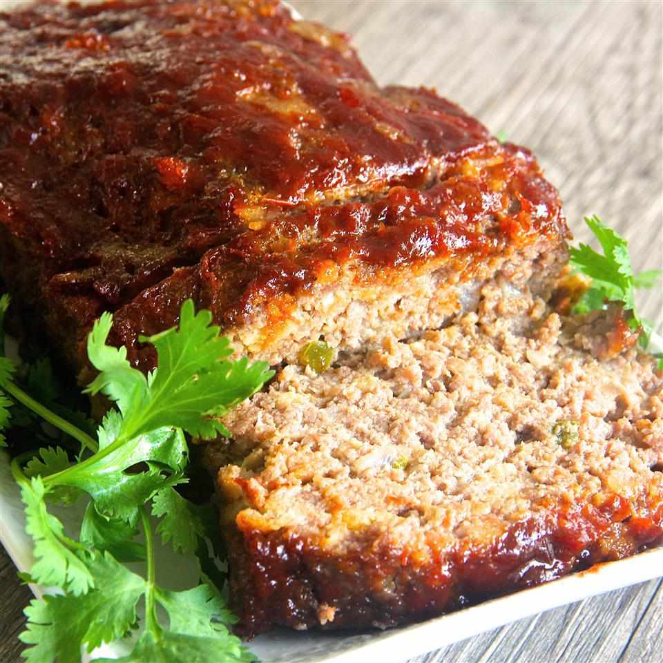a glazed meatloaf on a white ceramic platter with two slices cut, garnished with celery leaves