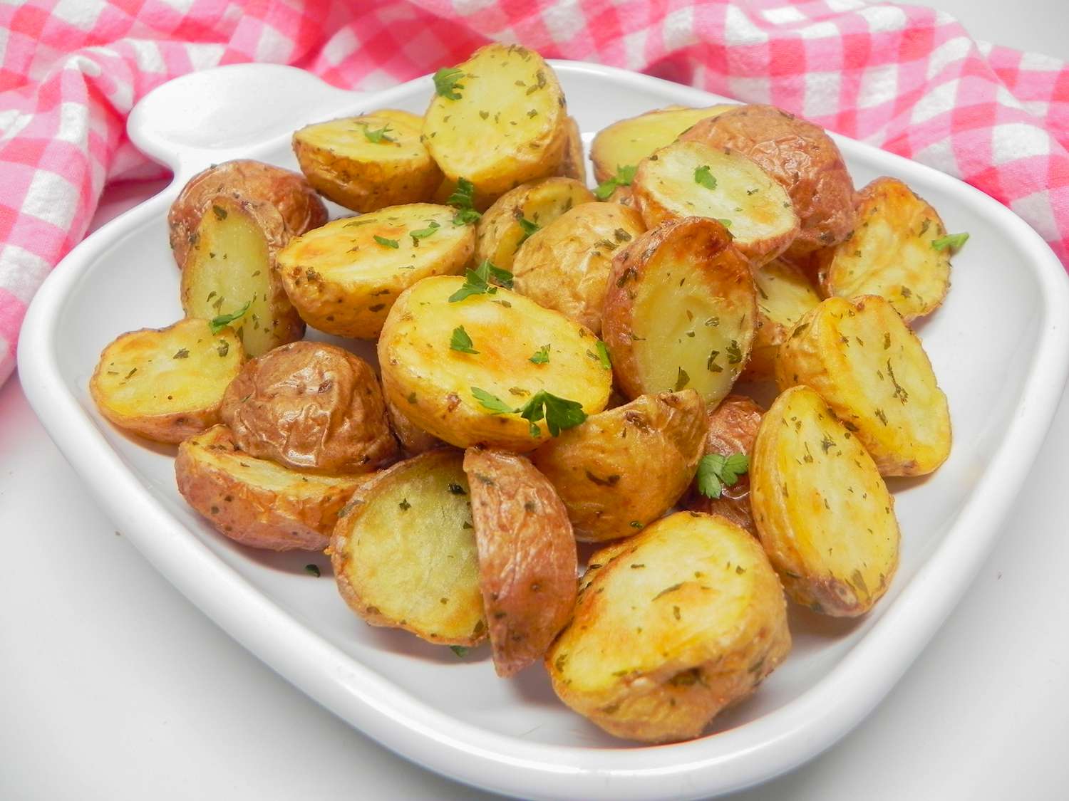 close up view of Air Fryer Garlic and Parsley Baby Potatoes on a white platter, with a red and white tablecloth in the background